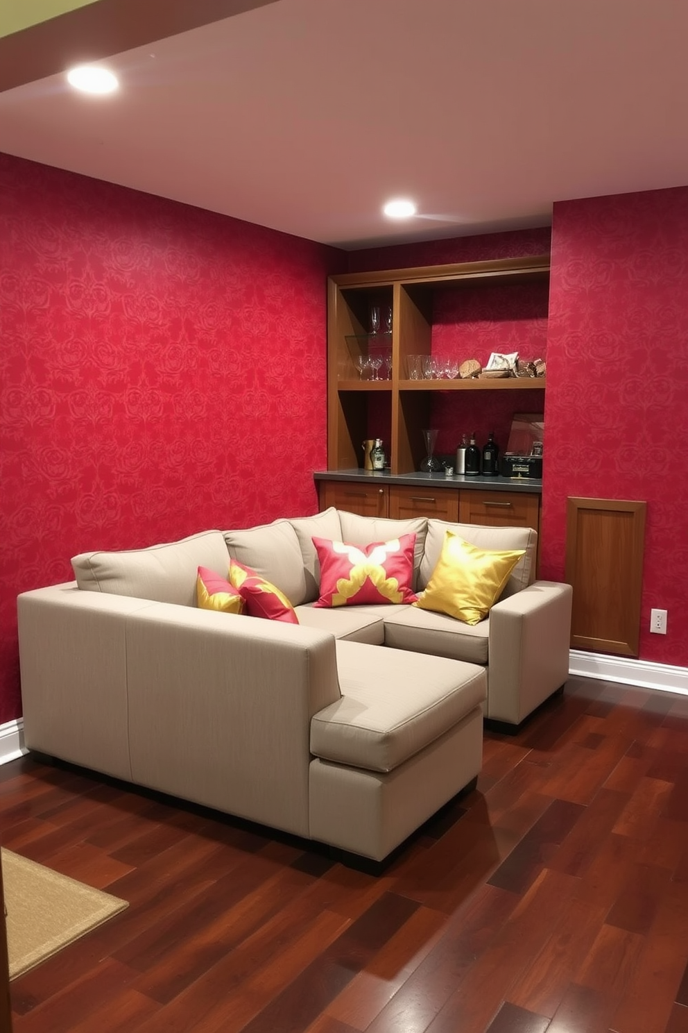 A cozy basement retreat featuring red patterned wallpaper that adds warmth and texture to the space. The room is furnished with a plush sectional sofa in a neutral tone, accented by vibrant red and gold throw pillows. In one corner, a small bar area showcases sleek wooden shelves filled with glassware and decorative items. The flooring is a rich dark wood, complementing the red wallpaper and creating an inviting atmosphere for relaxation and entertainment.