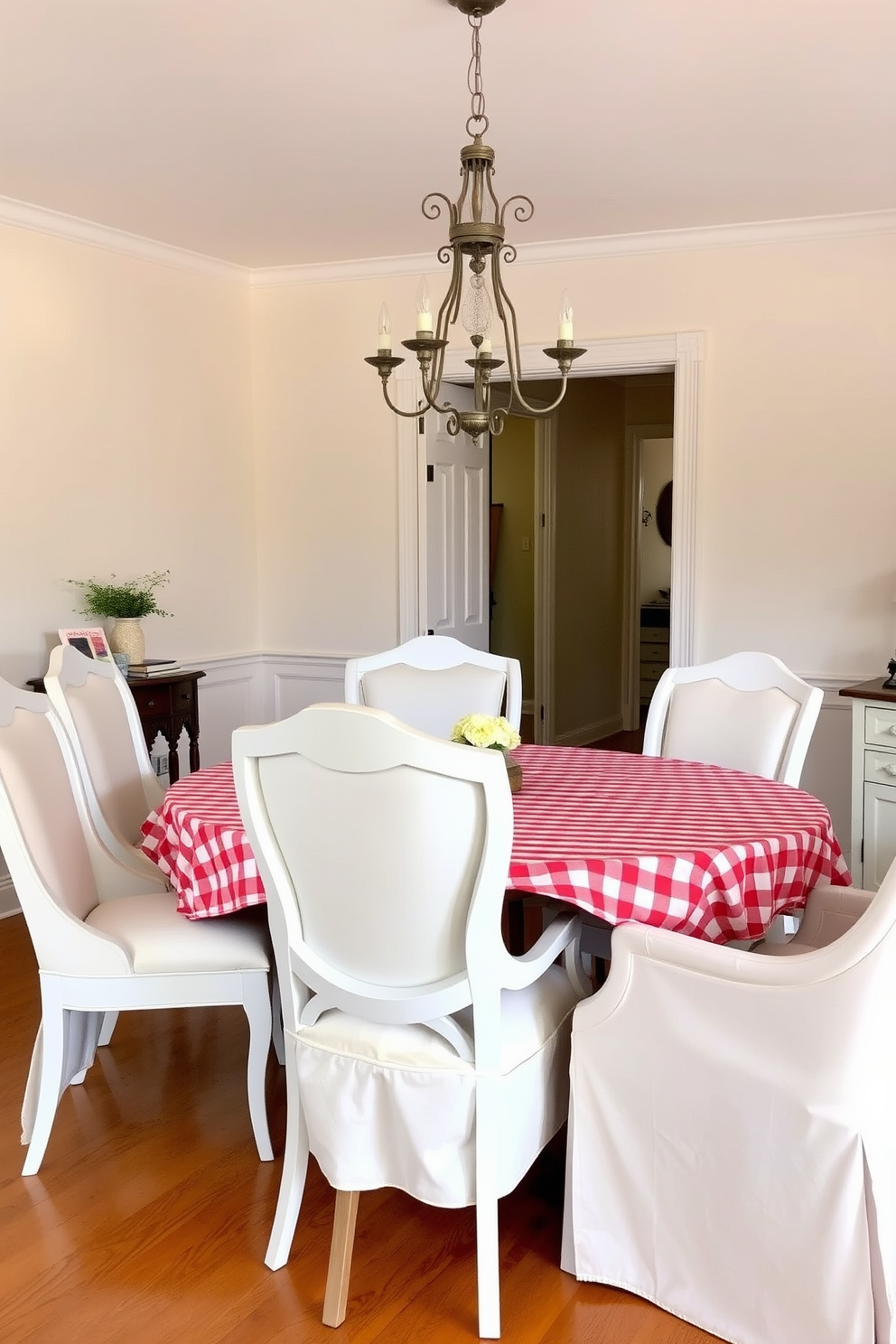 A charming dining room featuring a red and white checkered tablecloth draped over a rustic wooden table. Surrounding the table are elegant white chairs with soft cushioning, creating a warm and inviting atmosphere. The walls are painted in a soft cream color, enhancing the room's brightness and openness. A vintage chandelier hangs from the ceiling, adding a touch of sophistication to the overall design.