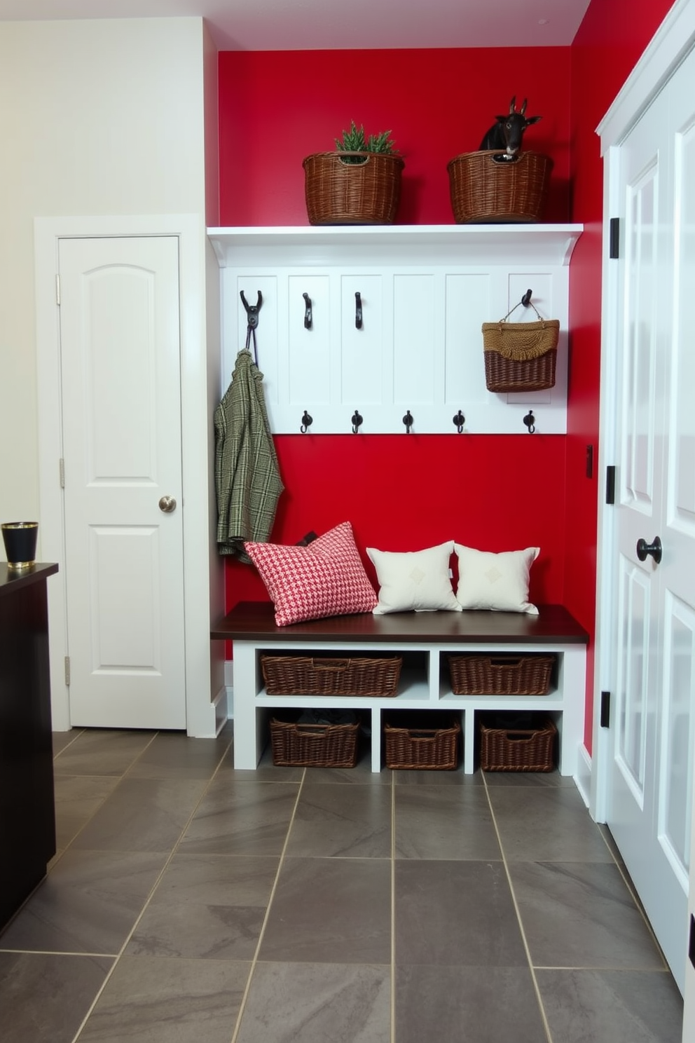 Bright red accent wall with hooks. The mudroom features a spacious layout with a built-in bench for seating and storage below. The floor is tiled with large gray ceramic tiles for easy maintenance. A stylish coat rack is mounted on the wall, complemented by decorative baskets for organization.