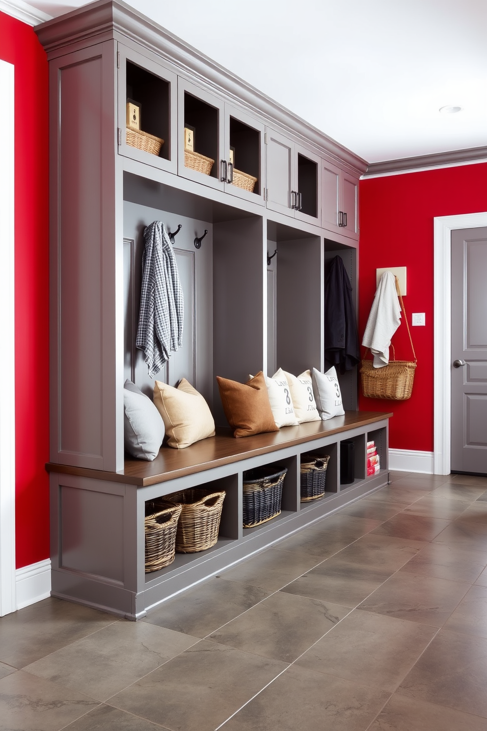 A stylish mudroom featuring a red and gray color scheme. The walls are painted a warm red, complemented by gray cabinetry and a bench with plush cushions. The floor is adorned with large gray tiles, providing durability and style. Hooks for coats and baskets for storage are neatly arranged, adding functionality to the space.