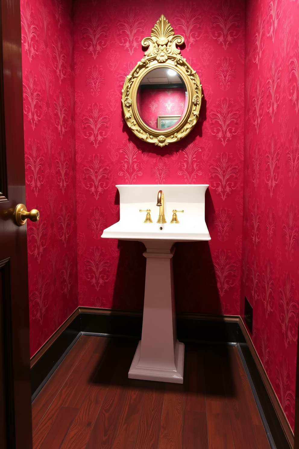 Sophisticated red wallpaper with a damask pattern adorns the walls of a luxurious powder room. A sleek white pedestal sink is complemented by a vintage-inspired gold faucet, creating an elegant focal point. The floor features dark hardwood planks that contrast beautifully with the vibrant wallpaper. A small round mirror with an ornate gold frame hangs above the sink, enhancing the room's opulence.