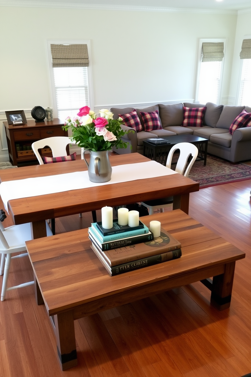 A farmhouse style dining table made of reclaimed wood is the centerpiece of the room, surrounded by mismatched chairs that add character. The table is set with a simple white tablecloth and a centerpiece of fresh flowers in a vintage pitcher. The family room features a cozy arrangement of a large sectional sofa adorned with plaid throw pillows, creating an inviting atmosphere. A reclaimed wood coffee table sits in front, topped with a stack of rustic books and a couple of scented candles.