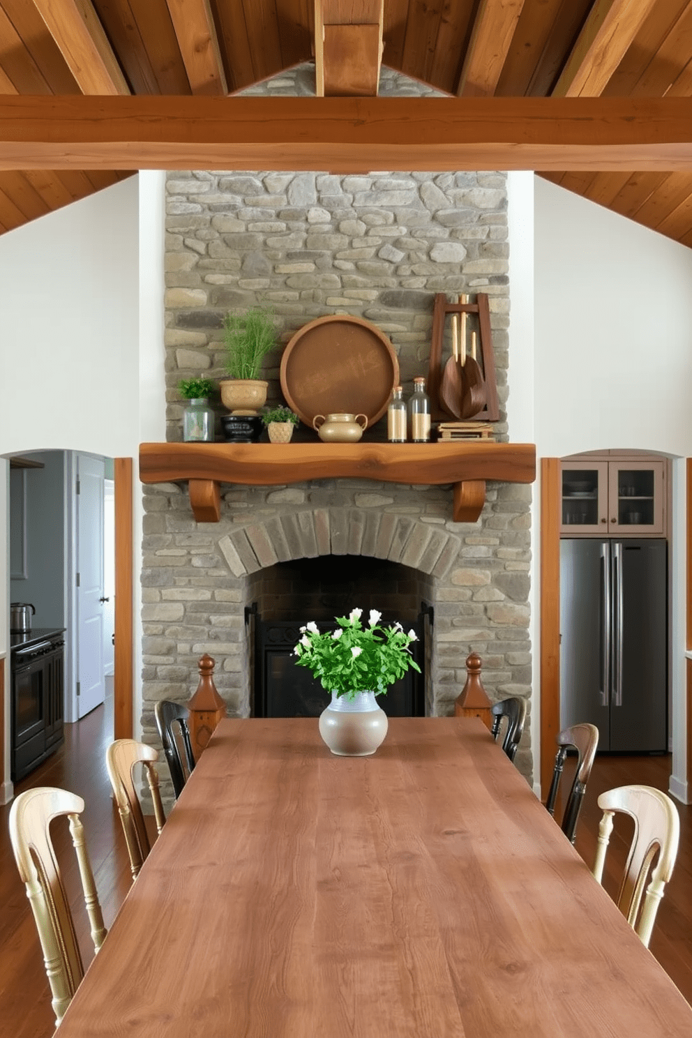 A rustic fireplace serves as the focal point in a cozy kitchen. The fireplace is made of reclaimed stone with a wooden mantel, adorned with decorative items and herbs in pots. The kitchen features exposed wooden beams on the ceiling and warm, earthy tones throughout. A large farmhouse table sits in the center, surrounded by mismatched chairs that add to the inviting atmosphere.