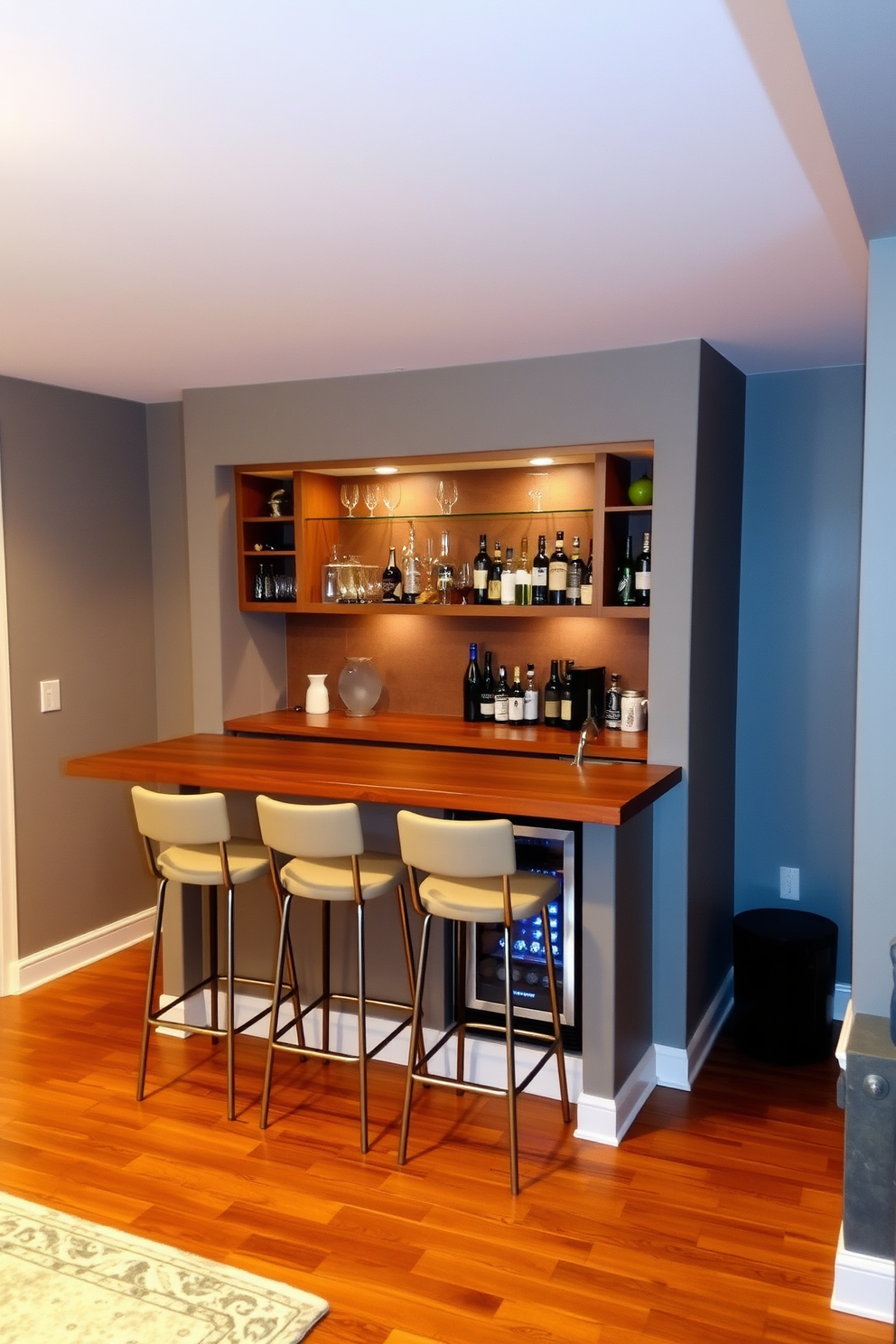 A cozy basement wet bar features a sleek wooden countertop with stylish bar stools arranged neatly underneath. The walls are painted in a warm gray hue, complemented by soft ambient lighting that creates an inviting atmosphere. Behind the bar, open shelving displays an array of glassware and decorative bottles, while a small fridge is tucked underneath for convenience. The flooring is a rich hardwood that adds warmth, and a plush area rug defines the seating area nearby.