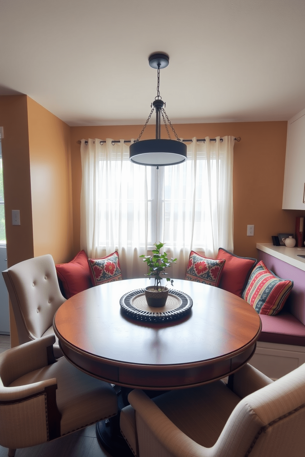 A cozy breakfast nook area features a round wooden table surrounded by plush upholstered chairs. Soft morning light filters through sheer curtains, illuminating a small potted plant on the table. The walls are painted in a warm, inviting color, and a built-in bench with colorful cushions provides additional seating. A charming pendant light hangs above the table, adding a touch of elegance to the simple kitchen design.