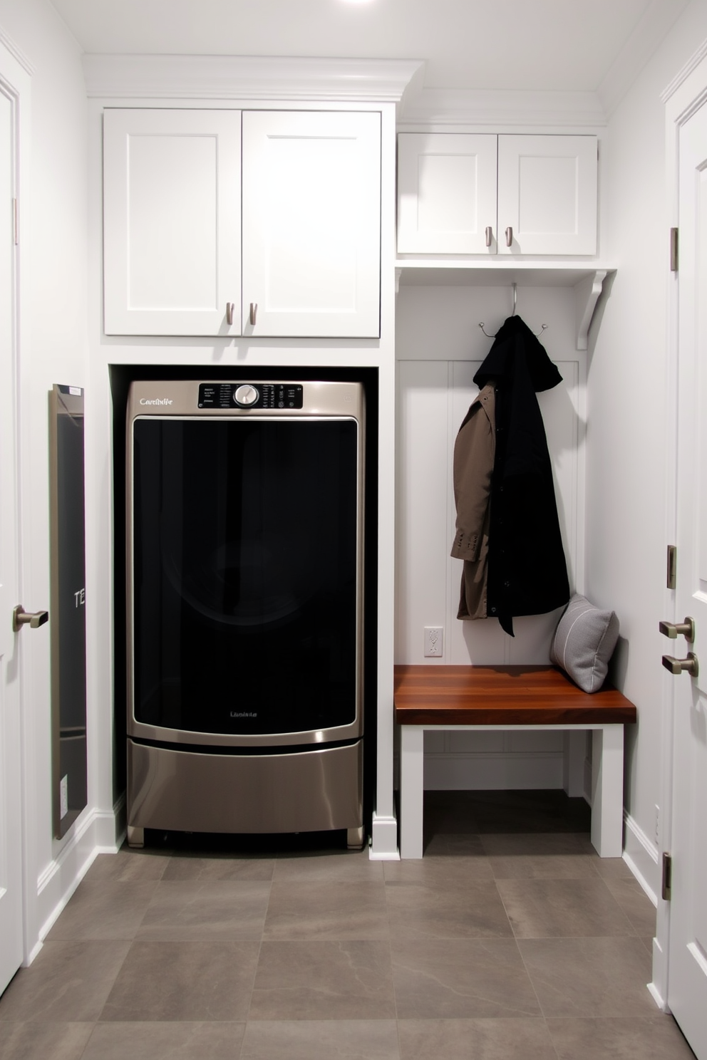 Integrated laundry area in mudroom. The space features a built-in washer and dryer with cabinetry above for storage. A bench with hooks for coats is positioned next to the laundry appliances. The walls are painted a crisp white, and the floor is covered in a durable gray tile.