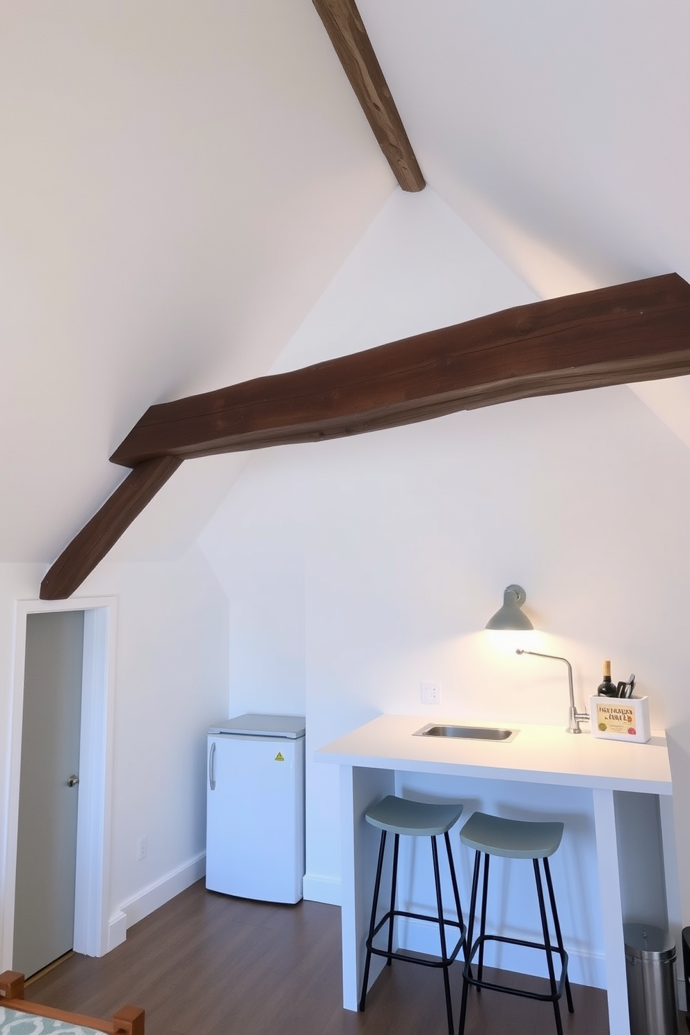 A cozy attic space designed for relaxation and functionality. The walls are painted in soft white, creating an airy feel, while exposed wooden beams add character and warmth. In one corner, a small kitchenette features a compact fridge and a sleek countertop with a sink. A few bar stools are placed at the counter, making it a perfect spot for casual dining or morning coffee.