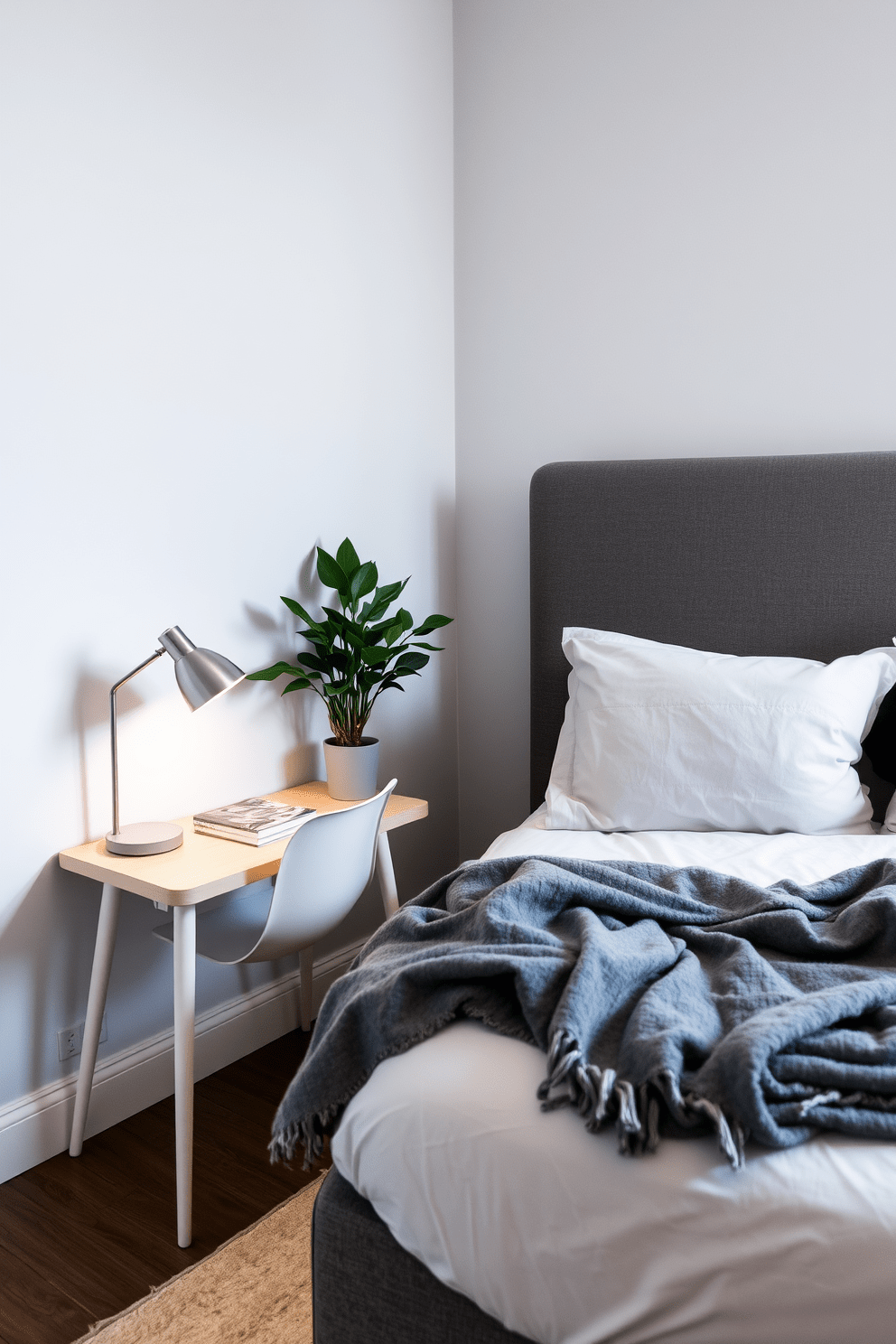 A cozy small bedroom with a compact desk for a functional work area. The bed is positioned against a light gray wall, and a soft, inviting throw is draped over the duvet. Next to the bed, a small bedside table holds a stylish lamp and a few books. The desk is placed in the corner, featuring a minimalist chair and a potted plant for a touch of greenery.