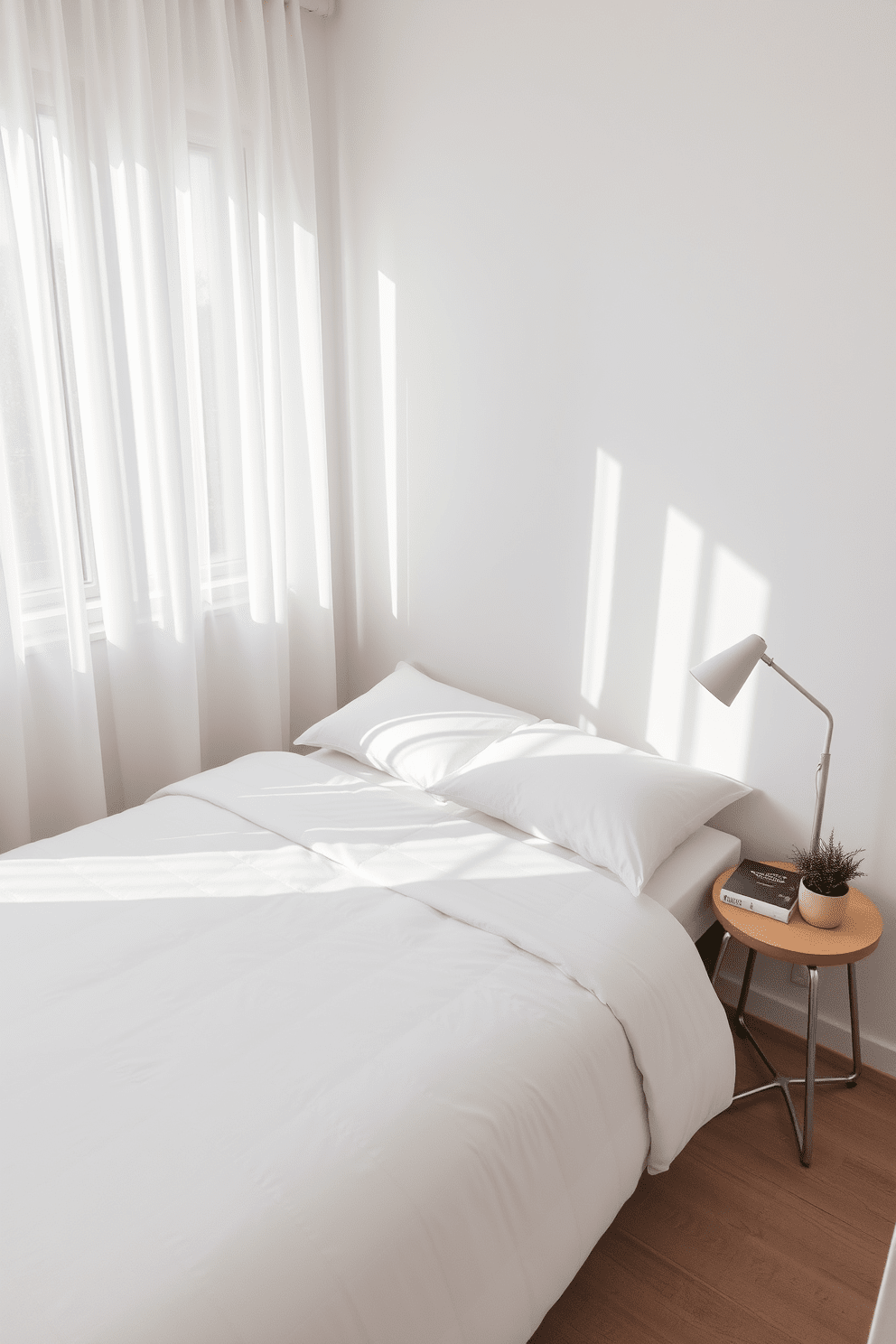 A cozy small bedroom featuring a minimalist bed with a simple white duvet and two matching pillows. The walls are painted in a soft neutral tone, and a small bedside table holds a sleek lamp and a book. Natural light filters through sheer curtains, creating a bright and airy atmosphere. A small potted plant sits in the corner, adding a touch of greenery to the serene space.