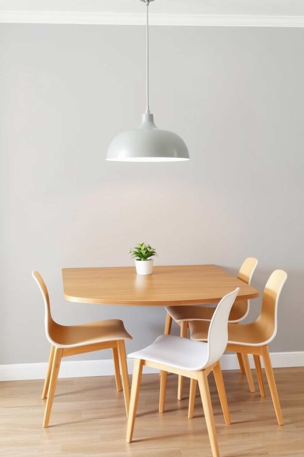 A wall-mounted drop-leaf table is elegantly positioned against a soft gray wall, providing a functional yet stylish dining solution. Surrounding the table are four sleek, modern chairs with light wood finishes that complement the table's design. The space is illuminated by a contemporary pendant light hanging above the table, adding warmth and sophistication. A small potted plant sits on the table, bringing a touch of greenery to the cozy dining area.