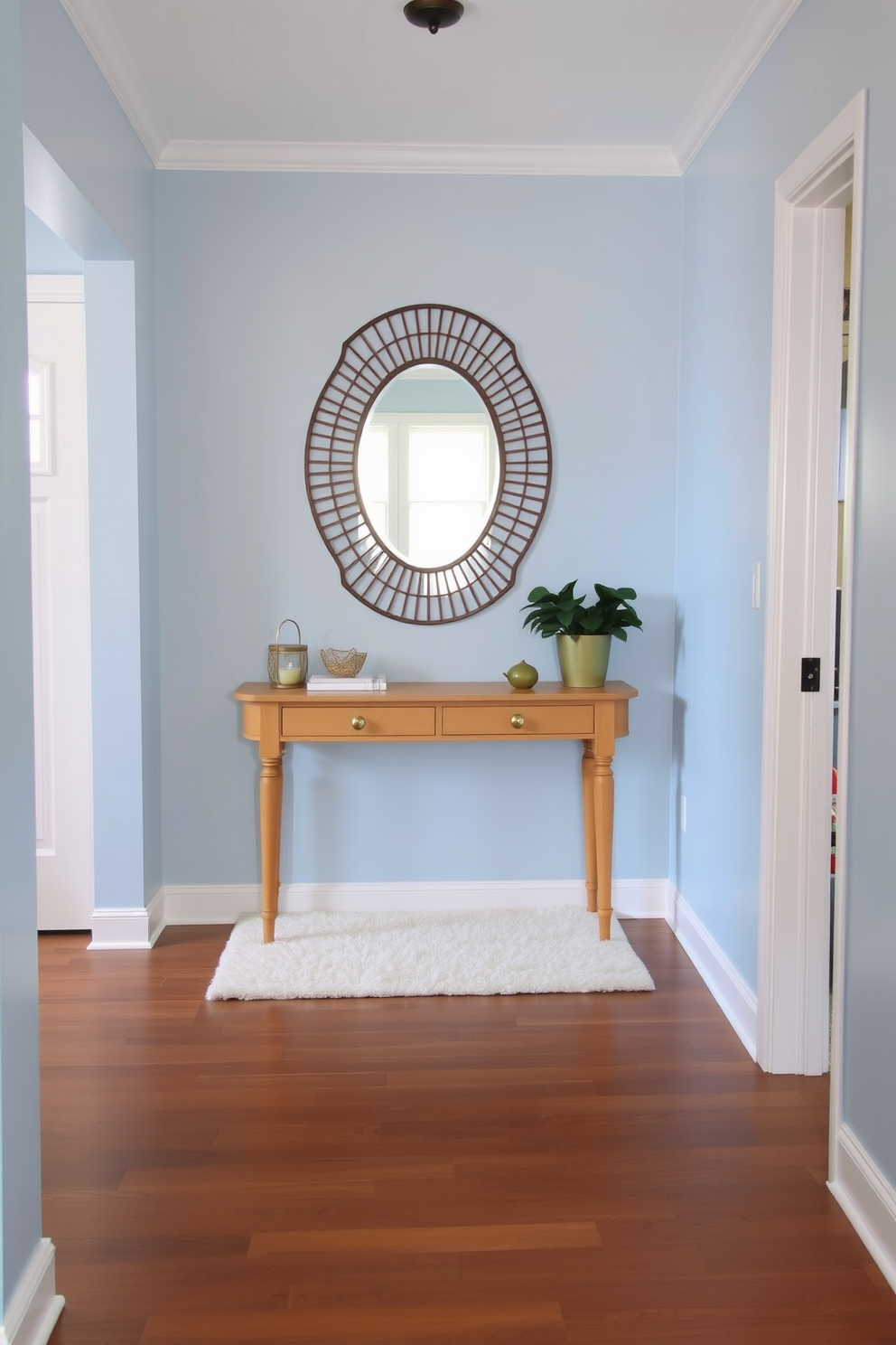 A small foyer featuring a soothing color palette of soft blues and warm neutrals. The walls are painted in a light sky blue, complemented by a natural wood console table adorned with a decorative mirror above it. A plush area rug in cream tones lies beneath the table, adding warmth to the space. A potted plant sits in the corner, enhancing the inviting atmosphere of the foyer.