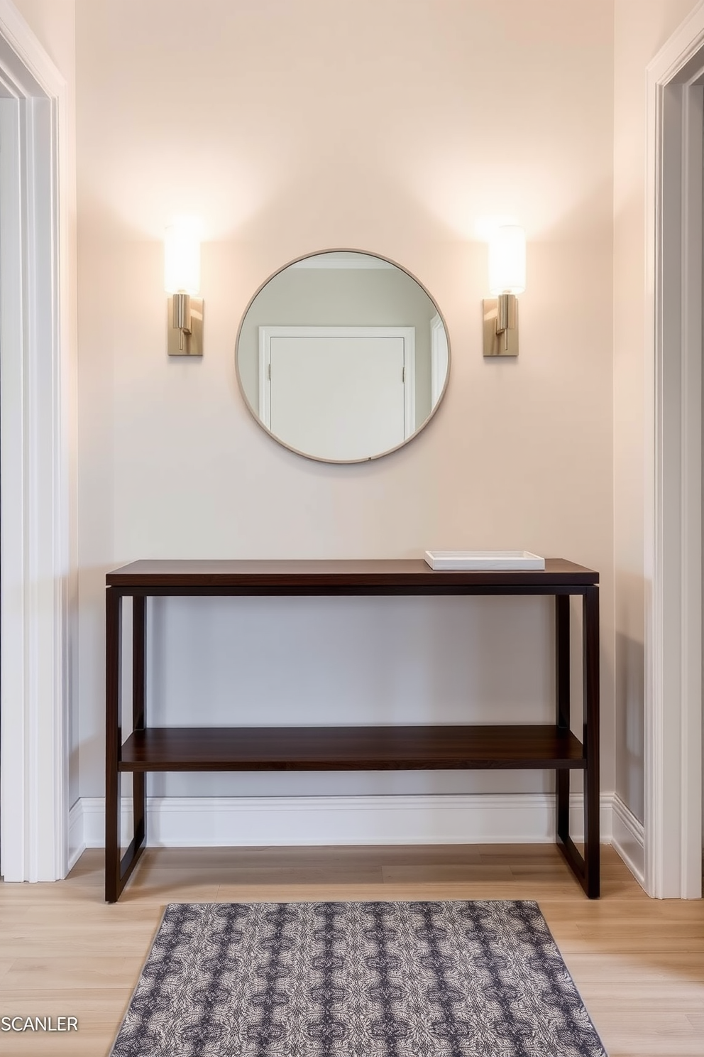 A small foyer features a sleek console table made of dark wood against a light gray wall. Above the table, two elegant wall-mounted lighting fixtures illuminate the space, casting a warm glow. The floor is adorned with a chic patterned rug that adds texture and color. A round mirror hangs above the console, reflecting the light and creating a sense of depth in the compact area.