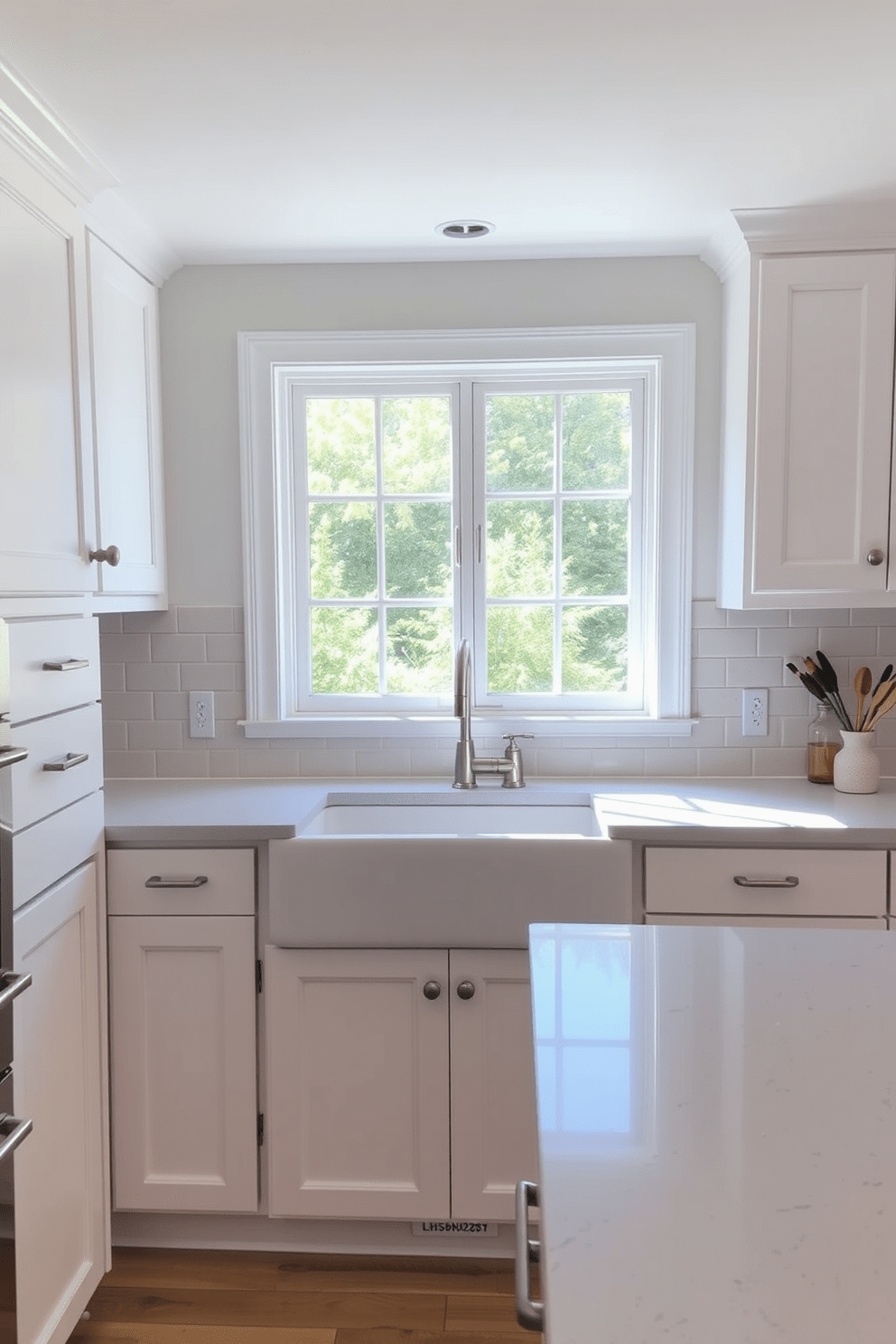 A cozy kitchen with a neutral palette that exudes serenity. The cabinetry is a soft white with brushed nickel handles, and the countertops are a light gray quartz. A farmhouse sink is centered beneath a large window, allowing natural light to flood the space. The backsplash features subtle beige subway tiles that complement the overall color scheme.