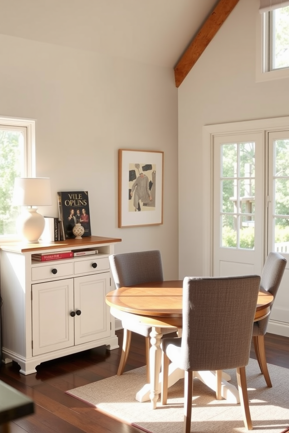 A cozy kitchen dining area featuring a small sideboard for storage. The sideboard is painted in a soft white color and adorned with decorative items like a vase and cookbooks. A round wooden dining table is placed in the center, surrounded by upholstered chairs in a muted gray fabric. Natural light floods the space through a large window, enhancing the warm and inviting atmosphere.