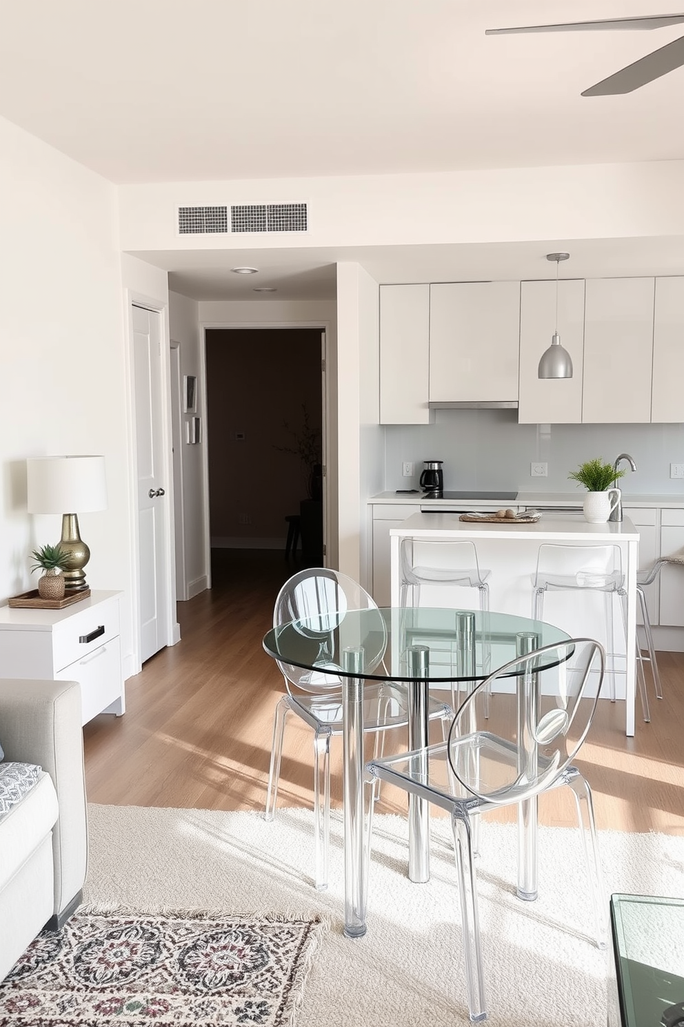 A cozy small kitchen living room design features clear furniture to create an open and airy feel. The space includes a compact dining table with transparent chairs, allowing for easy movement and minimizing visual clutter. In the kitchen area, sleek cabinetry in a light color complements the clear furniture. A stylish island with a glass top serves as both a prep space and a casual dining spot.