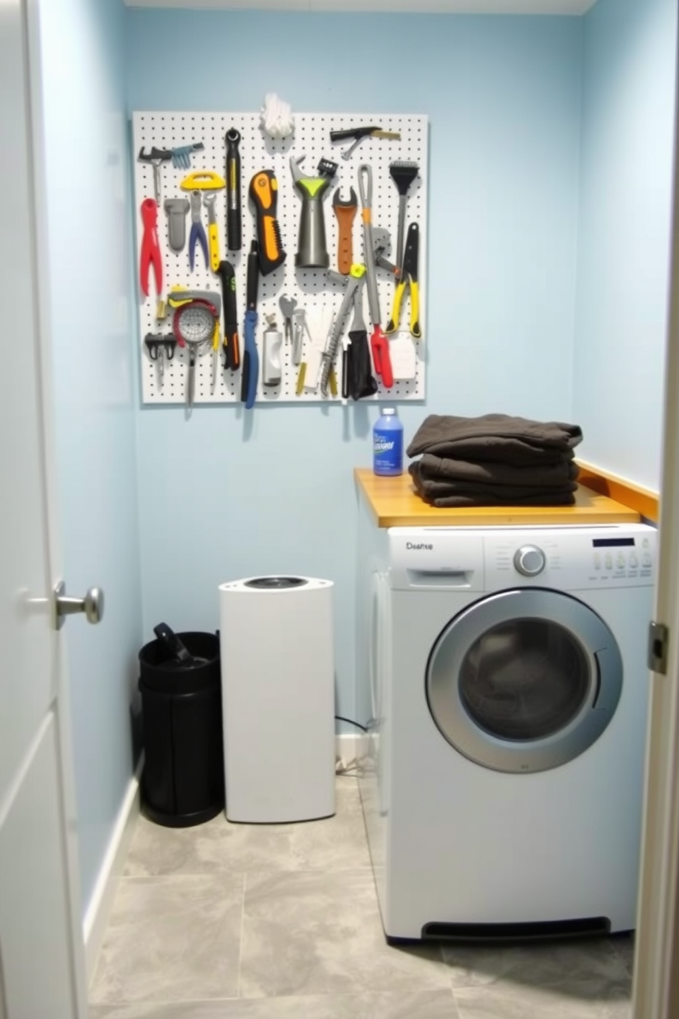 A small laundry room featuring a pegboard for tool storage. The walls are painted in a soft blue hue, and the floor is covered with light gray tiles. On the pegboard, various tools and accessories are neatly organized, creating an efficient workspace. To the right, a compact washer and dryer are stacked, with a wooden countertop above for folding clothes.