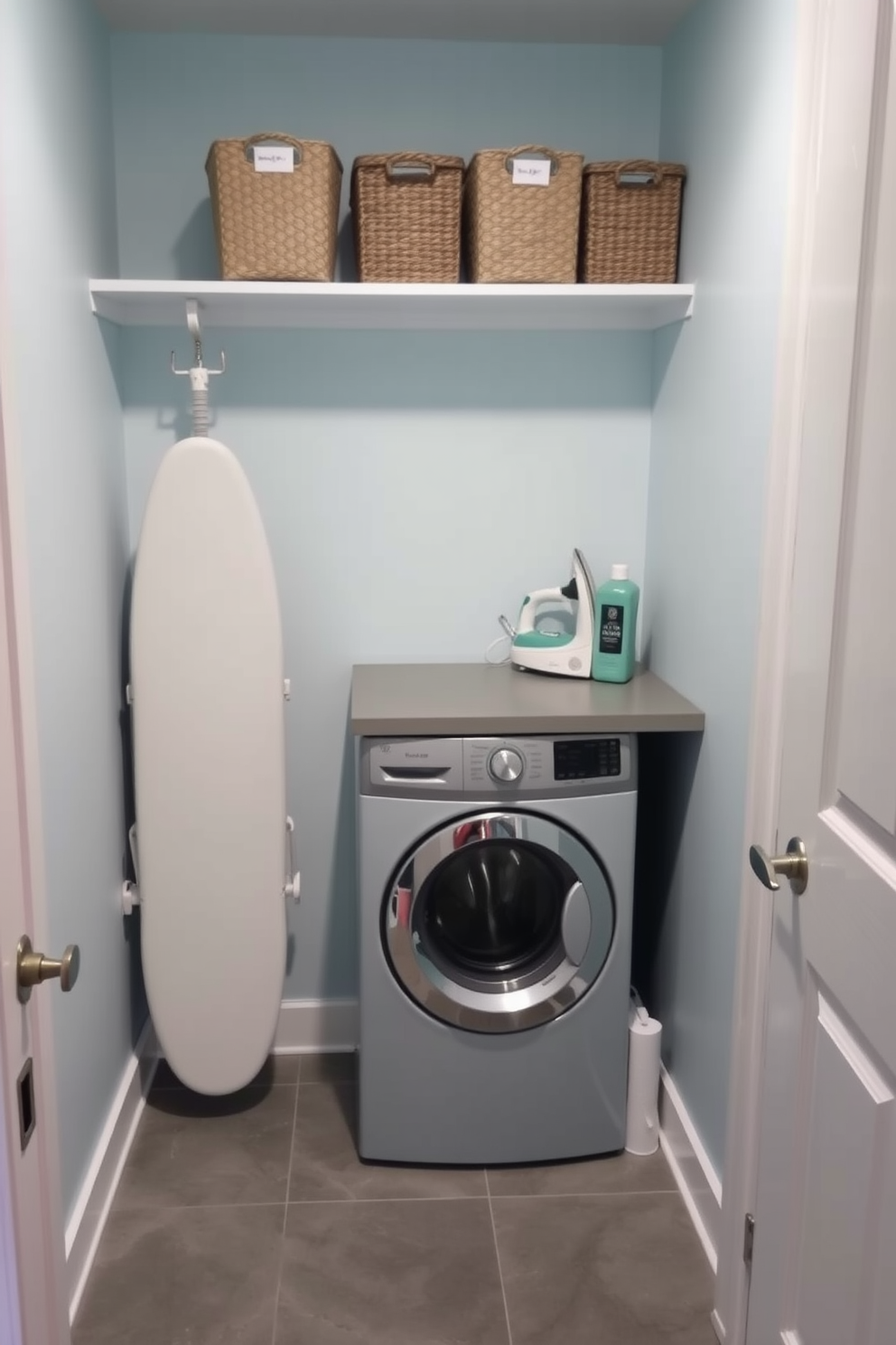 A cozy laundry room featuring a compact ironing board station tucked neatly into a corner. The walls are painted in a soft light blue, and the floor is covered with a durable gray tile that complements the space. A stackable washer and dryer are positioned beside a small countertop for folding clothes. Above the countertop, open shelving displays neatly organized laundry supplies and decorative baskets for added storage.