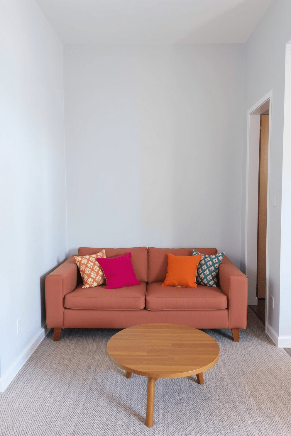 A narrow sofa is placed against the wall to maximize walking space in the small living room. The color of the sofa complements the light gray walls, creating a cozy and inviting atmosphere. A round coffee table sits in front of the sofa, providing a functional surface without overwhelming the space. Decorative pillows in vibrant colors add a pop of interest and comfort to the seating area.