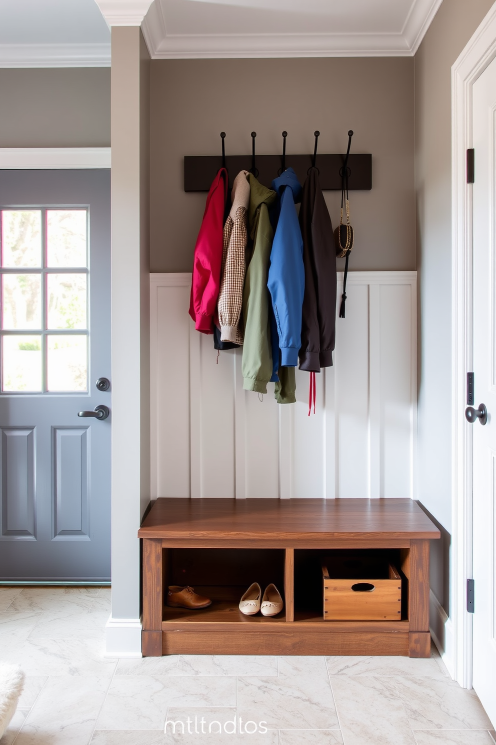 A cozy mudroom featuring a built-in bench with hidden storage beneath the seat. The walls are painted in a soft gray hue, and a stylish coat rack hangs above the bench, adorned with neatly organized jackets and accessories.