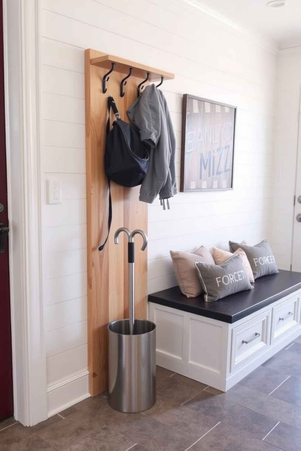 A small coat rack made of natural wood stands against the wall, providing a warm and inviting touch. Below the rack, an umbrella stand in a sleek metal finish offers a practical solution for rainy days. The mudroom features a combination of shiplap walls and a durable tile floor, creating a stylish yet functional space. A built-in bench with storage underneath complements the coat rack, making it easy to keep the area organized and tidy.