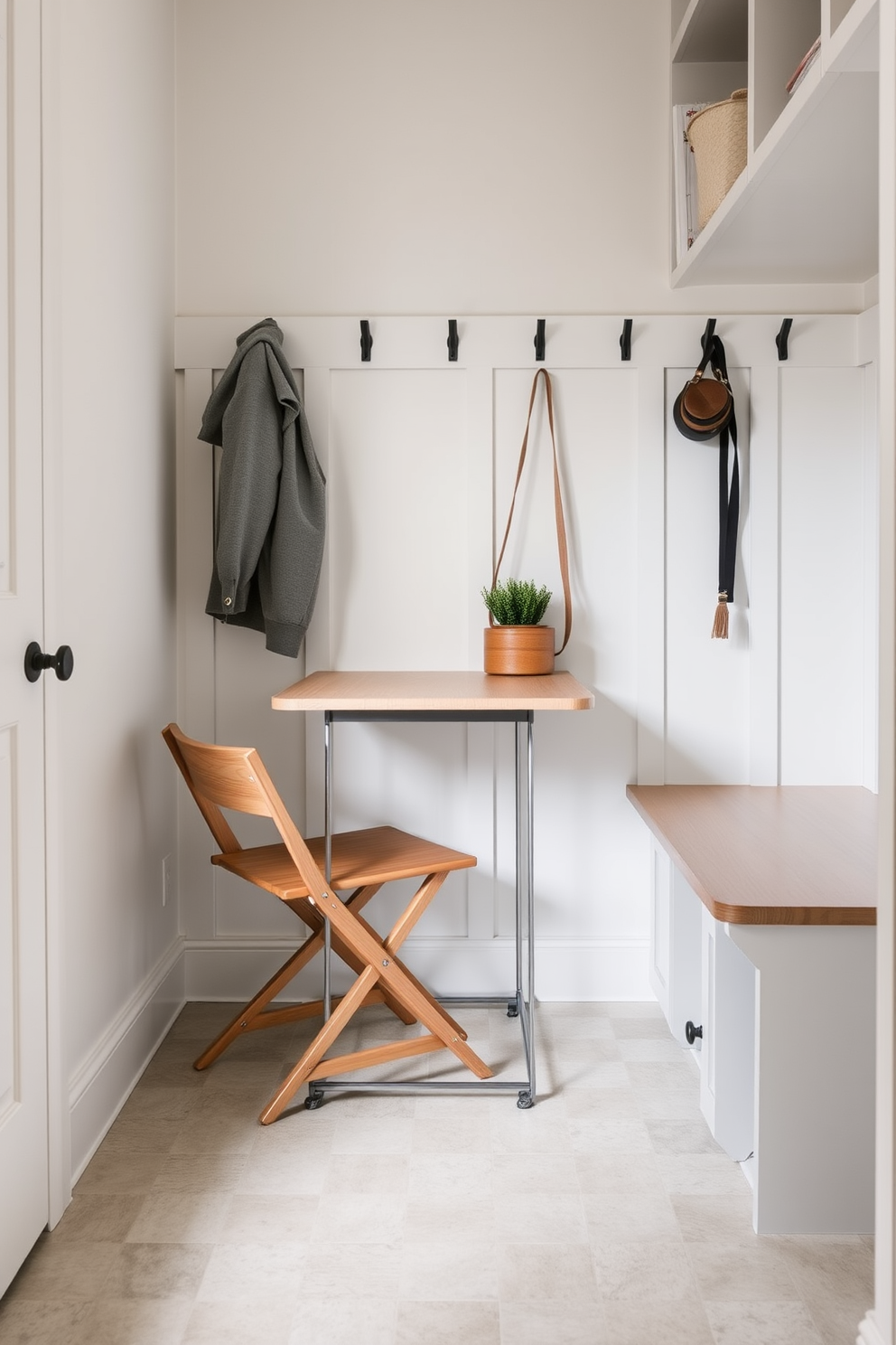 A compact foldable table is set against a light-colored wall, perfect for quick tasks and versatile use. The table features a sleek design with a natural wood finish, complemented by a comfortable chair tucked neatly underneath. The small mudroom is designed with functional storage solutions, including built-in benches and hooks for coats. Soft, muted colors create a welcoming atmosphere, while durable flooring is easy to clean and maintain.