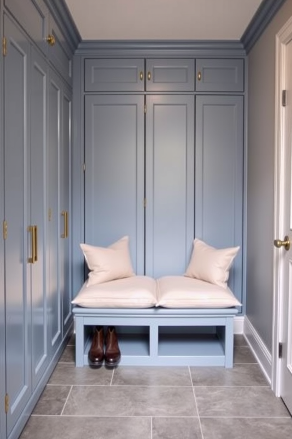 A cozy mudroom featuring built-in lockers for organized storage. The lockers are painted in a soft blue hue, with brass hardware adding a touch of elegance. A bench with plush cushions sits beneath the lockers, providing a comfortable spot to sit while removing shoes. The floor is covered in durable gray tiles, ideal for high traffic and easy cleaning.