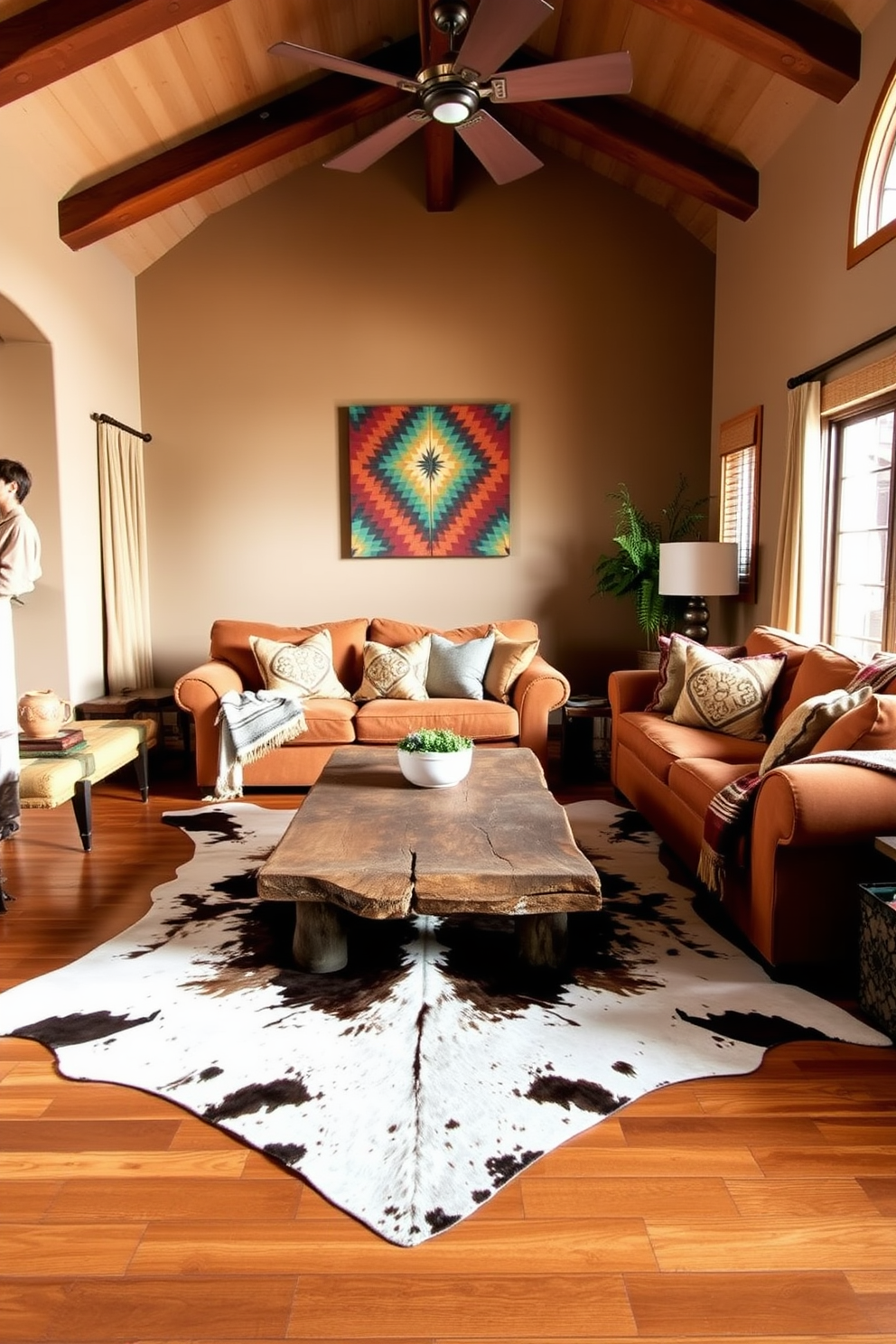 A cozy family room infused with Southwestern charm. The space features a large cowhide rug that adds warmth and texture to the hardwood floor, complemented by a rustic wooden coffee table at the center. Plush, oversized sofas in earthy tones create an inviting seating area. Colorful throw pillows and woven blankets enhance the Southwestern aesthetic, while a vibrant piece of wall art brings a focal point to the room.