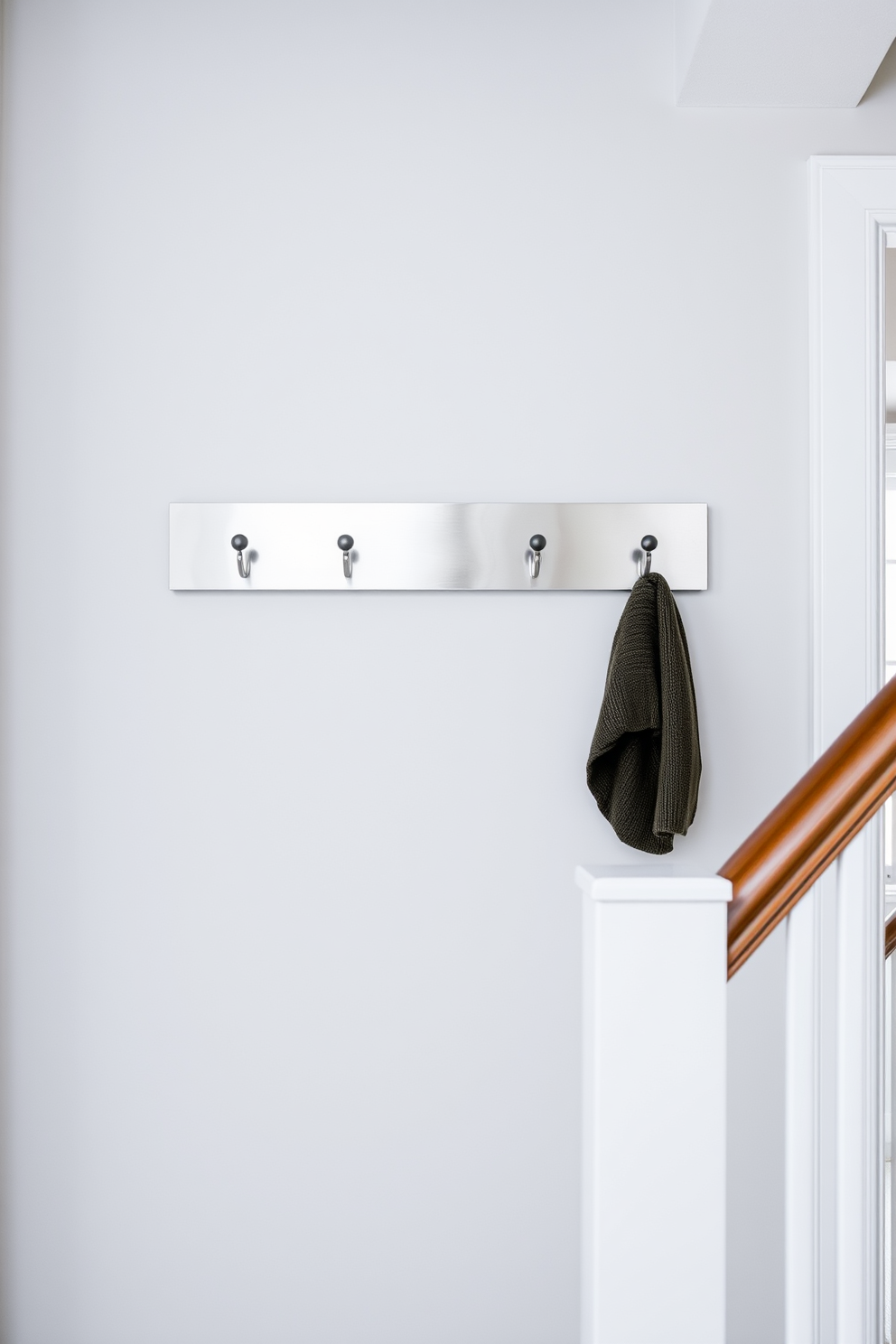 A stylish staircase landing featuring wall-mounted hooks for coats. The hooks are made of brushed nickel and are arranged neatly against a light gray wall, providing both functionality and a modern aesthetic.