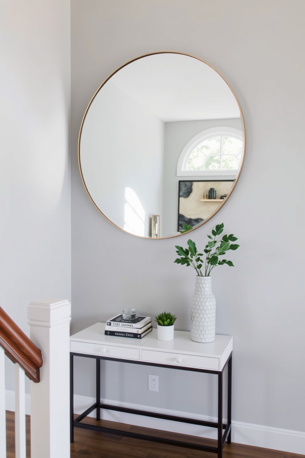 A stylish staircase landing features a large round mirror that reflects natural light, enhancing the sense of space. The walls are adorned with soft gray paint, complemented by a chic console table beneath the mirror, topped with decorative books and a small potted plant.