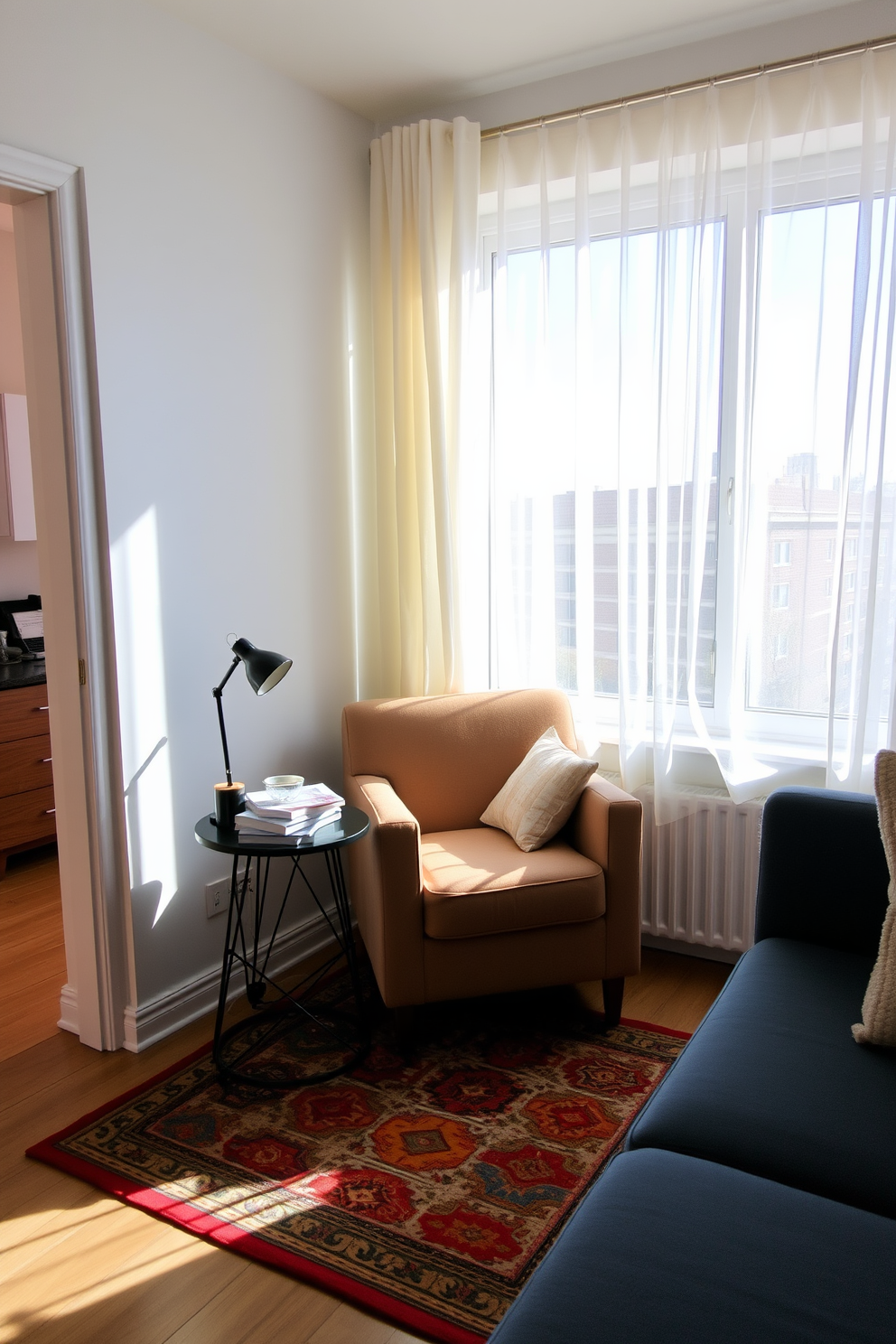 A cozy reading nook is nestled in the corner of a spacious studio living room. It features a plush armchair upholstered in soft fabric, accompanied by a small side table holding a stack of books and a warm cup of tea. Natural light pours in through a large window adorned with sheer curtains, creating a bright and inviting atmosphere. A colorful area rug lies beneath the chair, adding texture and warmth to the space.