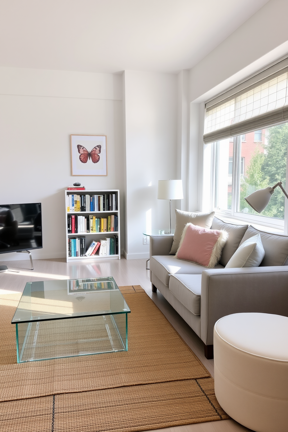 A bright and airy studio living room features soft white walls that reflect natural light. The space is furnished with a plush light gray sofa adorned with pastel throw pillows, complemented by a sleek glass coffee table. A cozy reading nook is created with a comfortable armchair in a light beige fabric positioned near a large window. A small bookshelf filled with colorful books adds a touch of personality, while a woven area rug ties the room together with warmth.