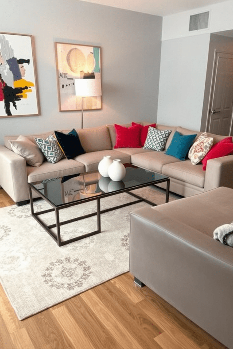 A stylish apartment setting featuring a large coffee table as the focal point. The coffee table is made of glass and metal, surrounded by a plush sectional sofa adorned with colorful throw pillows. The walls are painted in a soft gray, accented by abstract art pieces that add vibrancy to the space. A chic area rug in neutral tones anchors the seating area, while a modern floor lamp provides warm lighting.