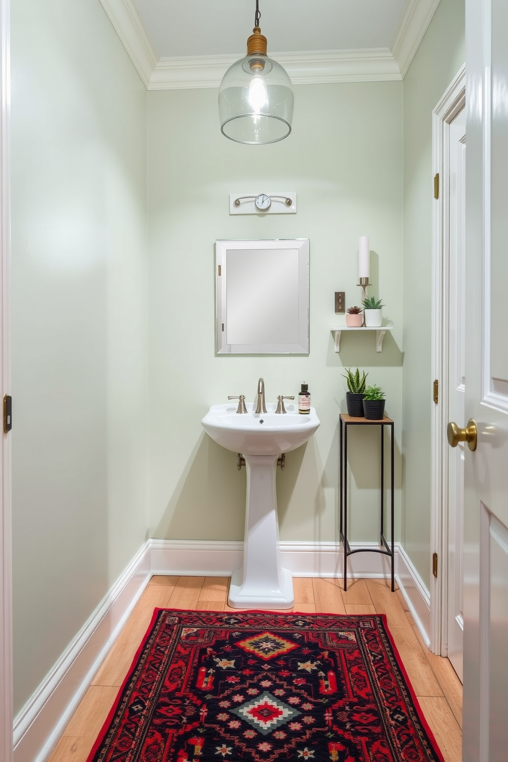 A cozy powder room featuring a compact design with a stylish pedestal sink and a sleek mirror above. The walls are painted in a soft pastel hue, and the floor is adorned with a vibrant, patterned rug that adds warmth and personality to the space. To the side, a small shelf displays decorative items such as candles and potted plants. A chic light fixture hangs from the ceiling, providing soft illumination that enhances the inviting atmosphere of the room.