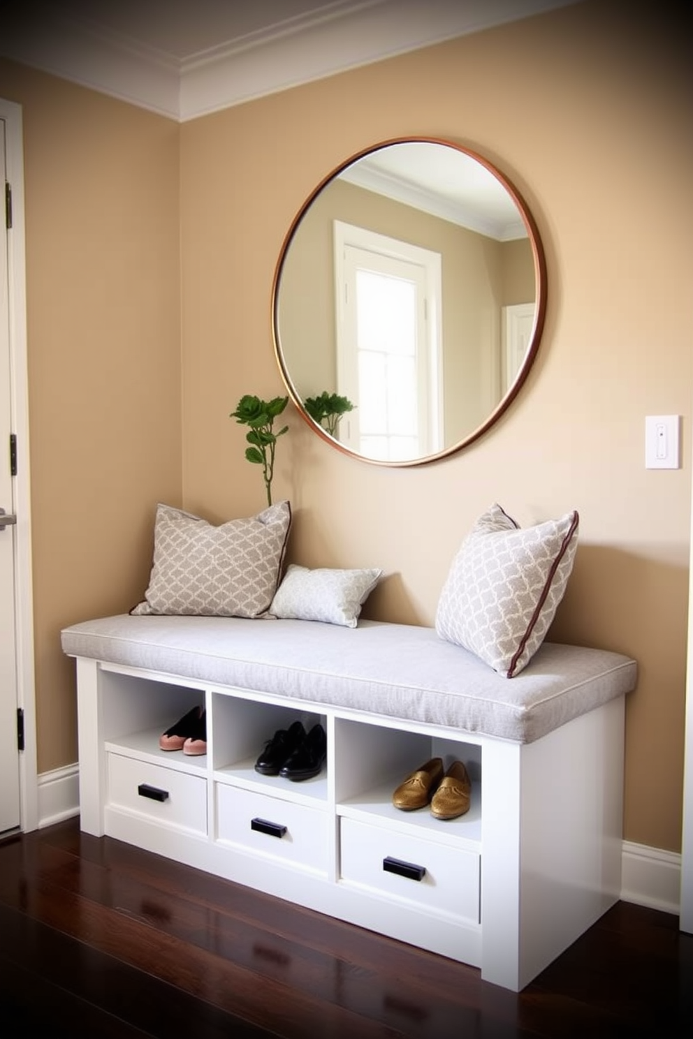 Cozy bench with storage underneath in a townhouse entryway. The bench is upholstered in a soft gray fabric and features built-in cubbies for shoes and accessories. The walls are painted in a warm beige tone, creating an inviting atmosphere. Above the bench, a large round mirror reflects natural light, while a small potted plant adds a touch of greenery.