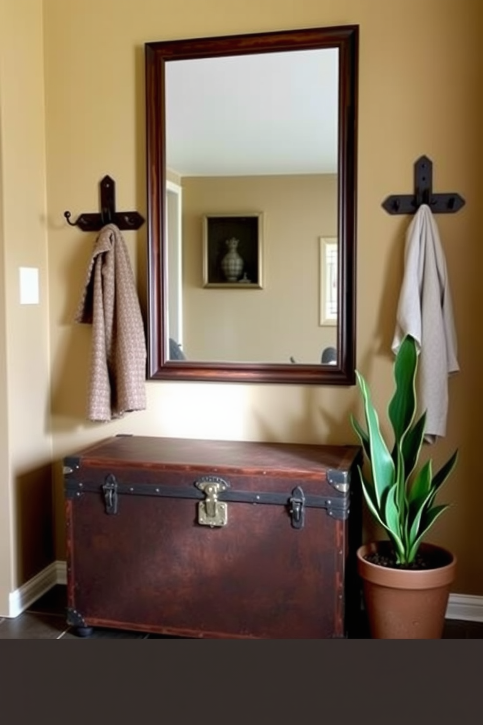 A vintage trunk serves as a stylish storage solution in the entryway. It is placed against the wall, complemented by a rustic coat rack and a large mirror above it. The walls are painted in a warm beige tone, creating a welcoming atmosphere. A small potted plant sits next to the trunk, adding a touch of greenery to the space.