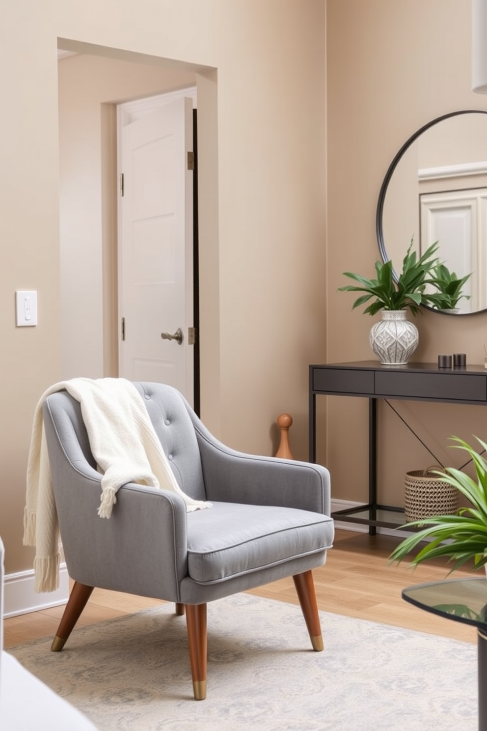 A stylish accent chair upholstered in soft gray fabric is placed in a cozy seating area. It features elegant wooden legs and is complemented by a plush throw blanket draped over one side. The townhouse entryway showcases a sleek console table with a decorative lamp and a large round mirror above it. The walls are painted in a warm beige tone, creating an inviting atmosphere for guests.