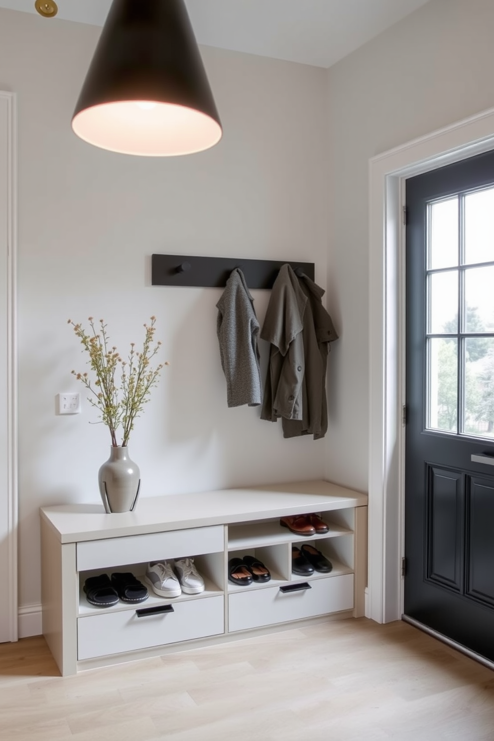 A sleek bench with shoe storage drawers is positioned against the wall in a modern townhouse entryway. The bench features a minimalist design with clean lines and is complemented by a stylish overhead light fixture that enhances the space's contemporary feel.