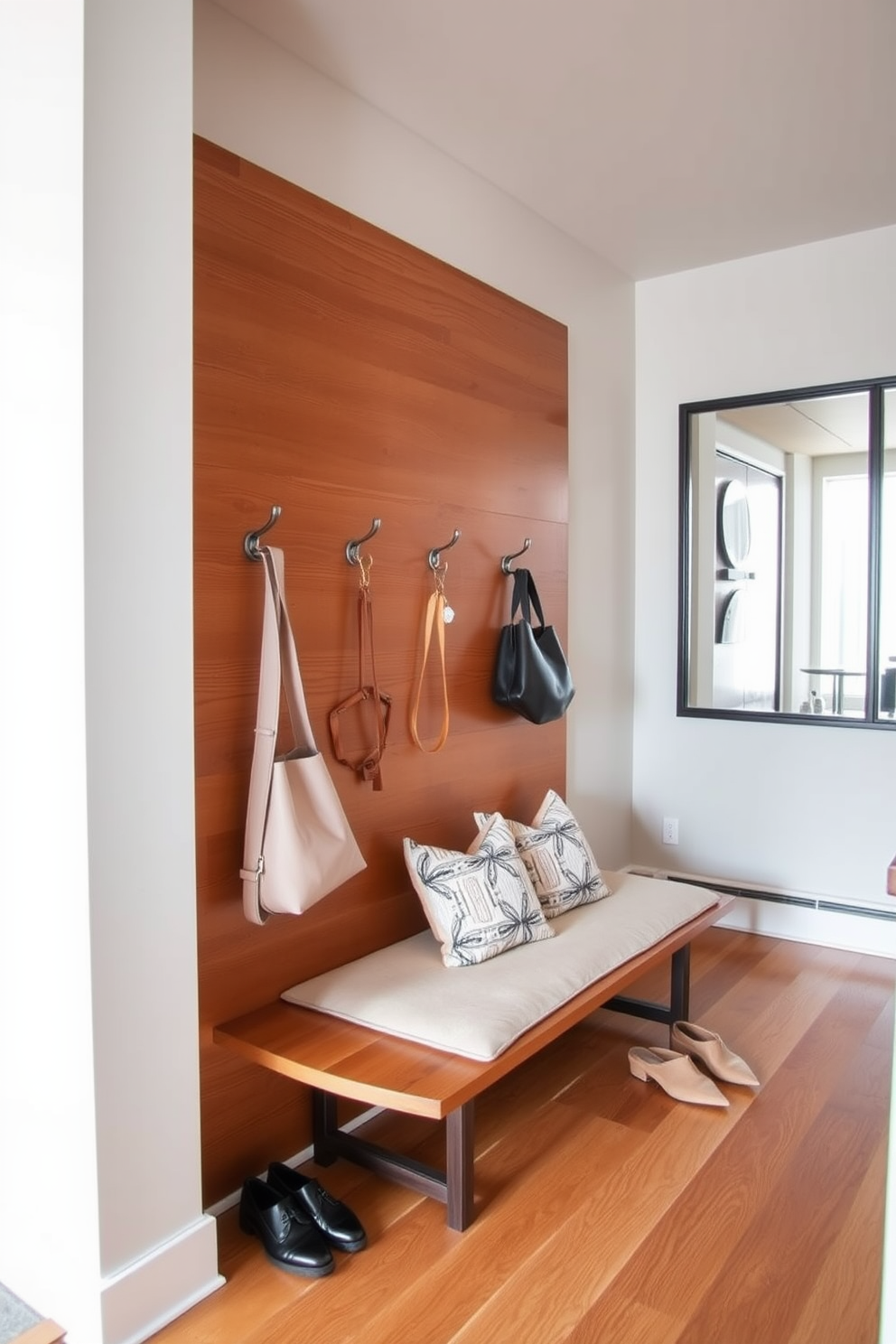 Stylish hooks for bags and accessories are mounted on a sleek wooden panel in a modern townhouse entryway. The hooks are arranged in a staggered pattern, complementing the warm tones of the hardwood floor and the soft, neutral walls. A plush bench with decorative cushions sits below the hooks, providing a cozy spot for putting on shoes. A large mirror with a minimalist frame hangs above the bench, reflecting natural light and enhancing the spacious feel of the entryway.