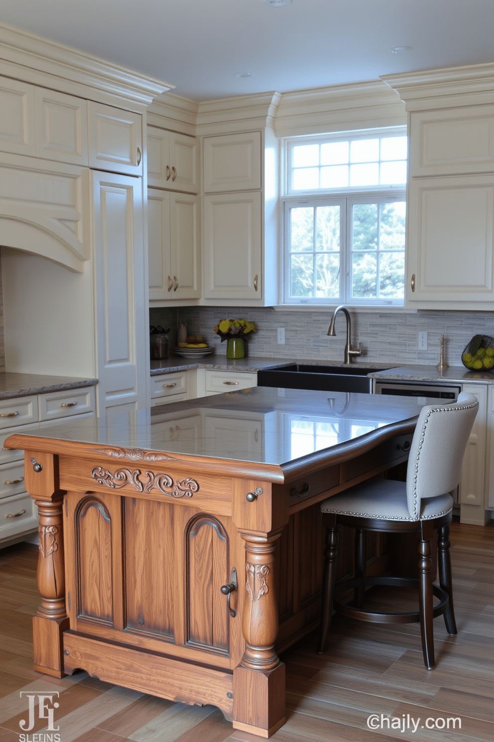 A charming kitchen featuring a furniture-style island made of reclaimed wood with intricate carvings. The island is topped with a polished granite surface and surrounded by high-backed stools upholstered in a neutral fabric. The cabinetry is painted in a soft cream color with antique brass hardware, complementing the warm tones of the island. A classic farmhouse sink sits beneath a window, allowing natural light to illuminate the space.