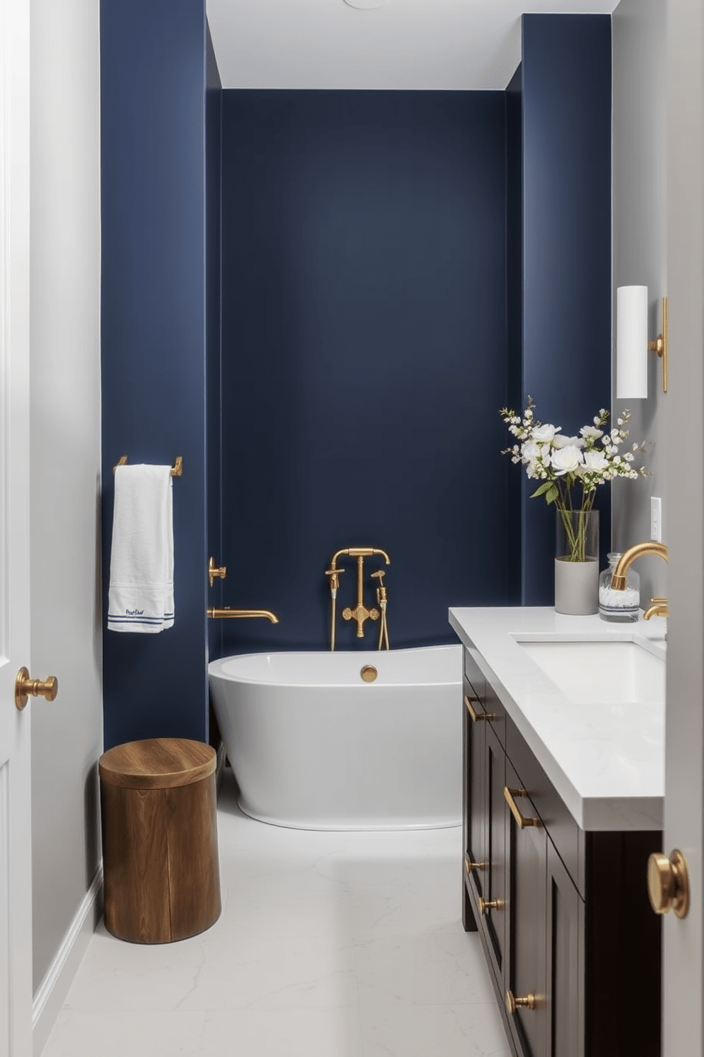 A striking accent wall painted in a bold navy blue creates a focal point in the bathroom. The surrounding walls are adorned with soft gray tones, complementing the modern fixtures and accessories. The bathroom features a freestanding soaking tub placed against the accent wall, enhancing the luxurious feel. Sleek brass fixtures and a stylish vanity with a white countertop complete the transitional design, blending contemporary and classic elements.