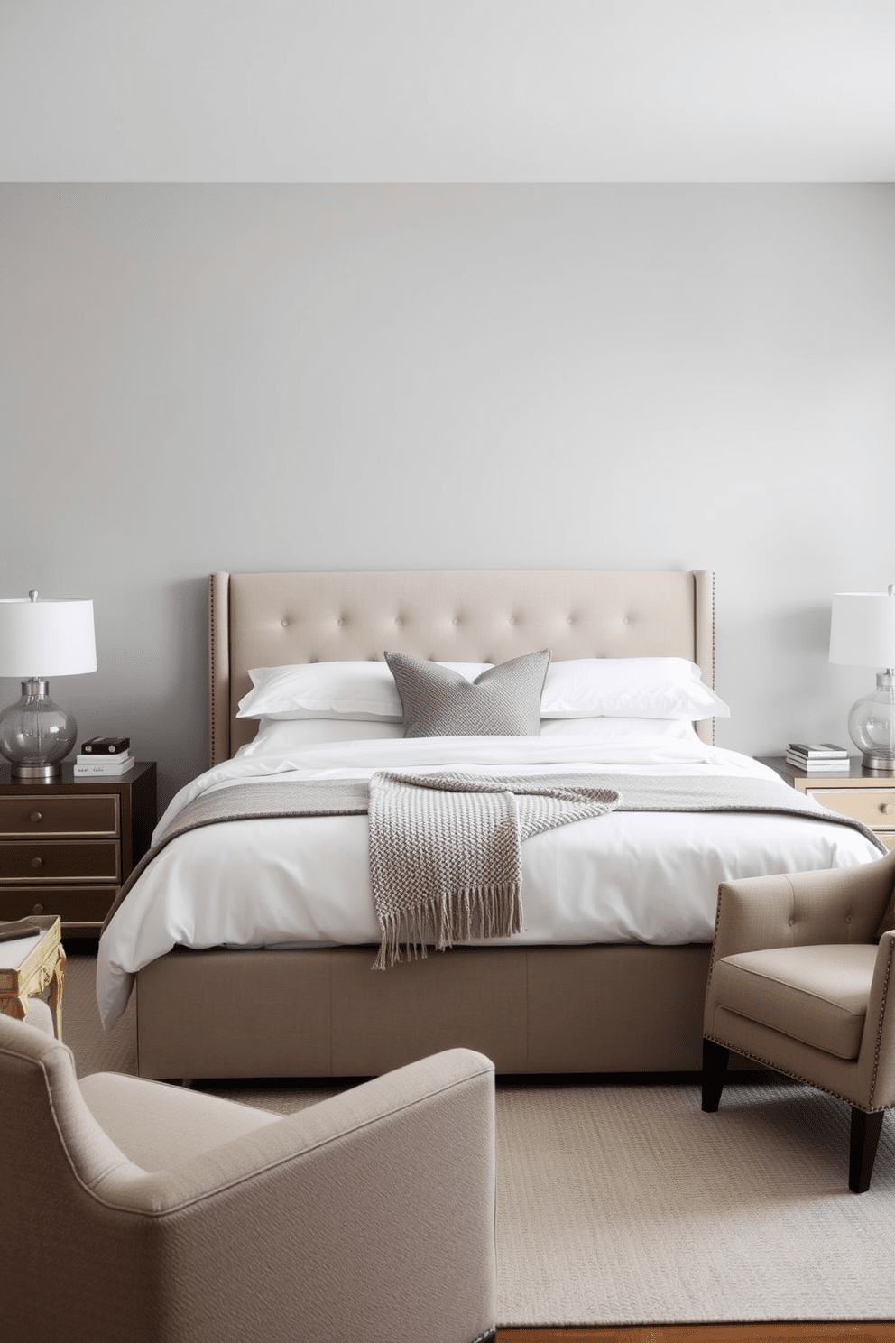 A serene transitional bedroom featuring a king-sized bed with a plush upholstered headboard centered against a soft gray wall. On either side of the bed, matching nightstands with elegant lamps create a sense of balance and harmony. The bedding is layered with crisp white linens and a textured throw blanket in muted tones. A cozy armchair sits in one corner, accompanied by a small side table, inviting relaxation and comfort.