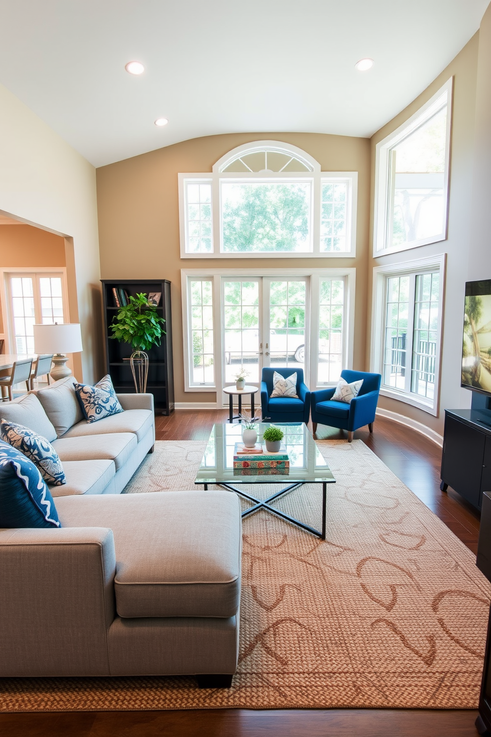 A transitional living room featuring a comfortable sectional sofa in a soft gray fabric, paired with a sleek glass coffee table at the center. The walls are painted in a warm beige tone, and large windows allow natural light to flood the space, complemented by layered lighting options for different moods. Accent chairs in a rich navy blue are positioned opposite the sofa, creating a cozy conversation area. A textured area rug anchors the space, while decorative throw pillows add pops of color and warmth to the overall design.