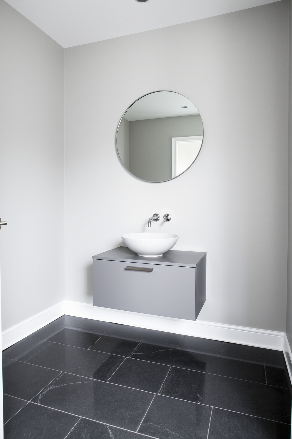 A sleek powder room featuring a monochromatic color scheme that emphasizes shades of gray. The walls are painted in a soft dove gray, while the floor showcases dark gray tiles with a glossy finish. A minimalist floating vanity in a matching gray tone holds a stylish vessel sink. Above the vanity, a large round mirror reflects the elegant simplicity of the space, complemented by subtle metallic accents.