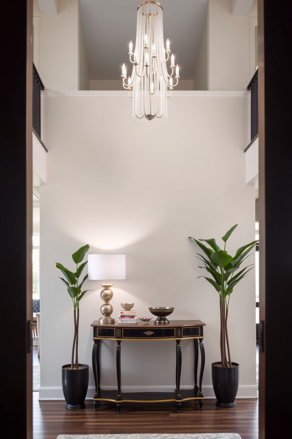 A decorative console table is elegantly placed against the wall in a two story foyer. The table is adorned with a stylish lamp, a stack of art books, and a decorative bowl, creating an inviting focal point. The foyer features a grand chandelier hanging from the high ceiling, illuminating the space with warm light. Tall potted plants flank the entrance, adding a touch of greenery and sophistication to the design.