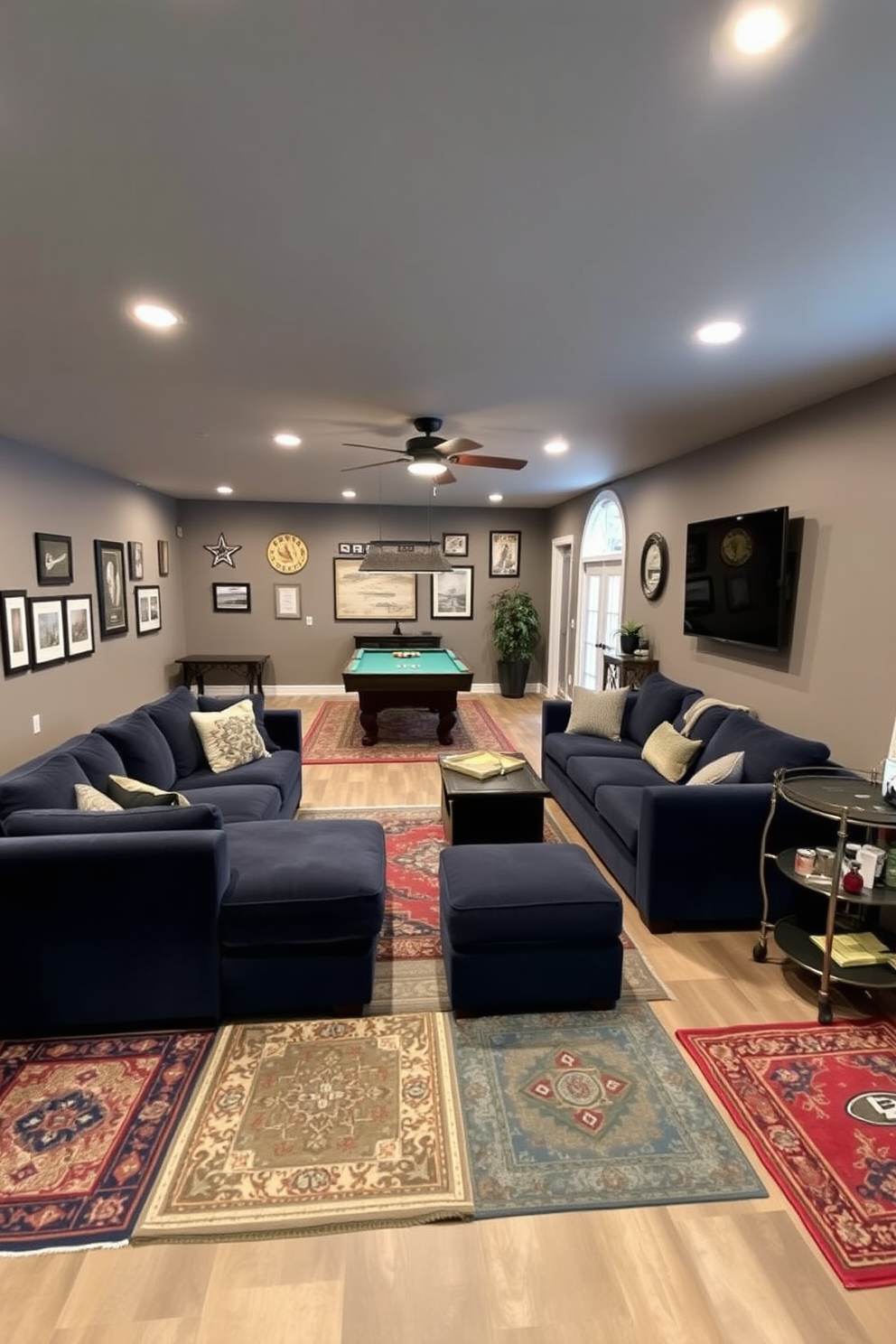 A cozy unfinished basement man cave featuring a large sectional sofa in a deep navy blue color. The space is divided by accent rugs that define different areas, including a game zone with a pool table and a relaxation corner with a bar cart. The walls are painted in a warm gray hue, and industrial-style lighting fixtures hang from the ceiling. Decor elements include framed sports memorabilia and a large flat-screen TV mounted on one wall for entertainment.