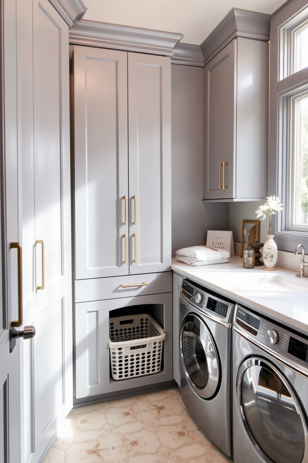 A functional utility room features laundry baskets seamlessly integrated into custom cabinetry. The cabinetry is painted in a soft gray hue, with sleek handles and ample storage space for cleaning supplies. The room includes a spacious countertop for folding clothes, adorned with stylish decor items. Natural light floods in through a window, illuminating the space and highlighting the organized, efficient design.