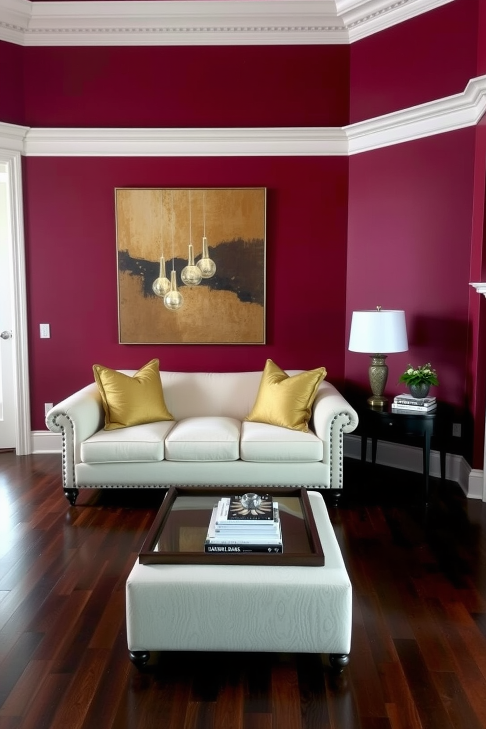 A living room featuring rich burgundy walls that create a dramatic and elegant atmosphere. The space is complemented by a plush cream-colored sofa adorned with gold accent pillows and a large abstract artwork that harmonizes with the wall color. The flooring consists of dark hardwood that adds warmth and depth to the room. A stylish coffee table in the center is topped with a decorative tray and a few carefully arranged books, enhancing the sophisticated ambiance.