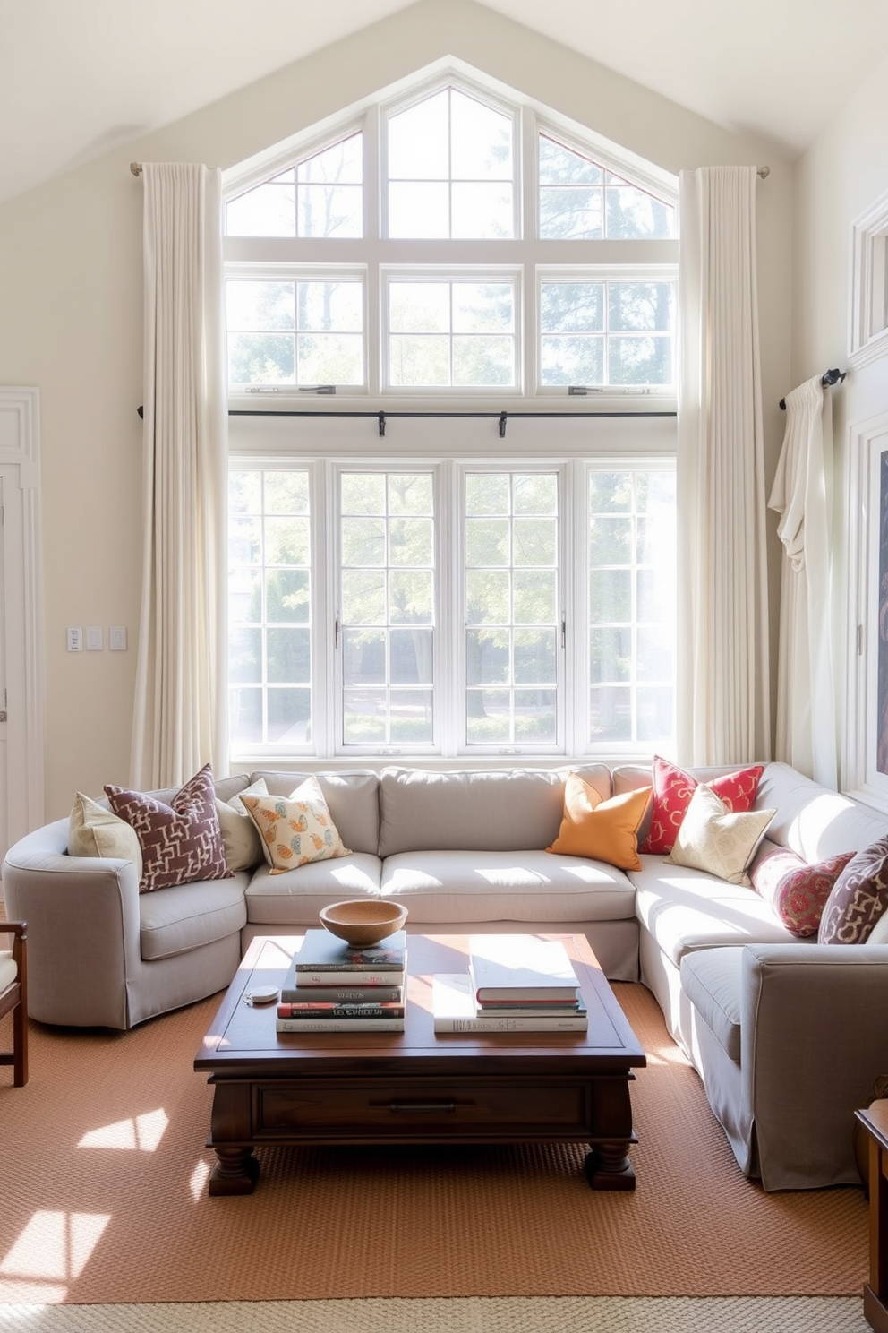 A bright and airy family room filled with natural light. Soft white drapes frame large windows, allowing sunlight to filter in gently. The room features a plush sectional sofa in a light gray fabric, complemented by a mix of colorful throw pillows. A wooden coffee table sits in the center, adorned with a stack of books and a decorative bowl.