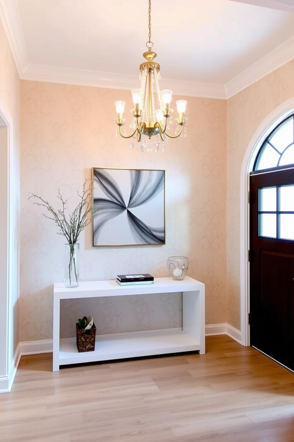 An elegant chandelier hangs gracefully above a sleek white console table, casting a warm glow across the foyer. The walls are adorned with soft beige wallpaper, complementing the light wood flooring and enhancing the airy feel of the space.