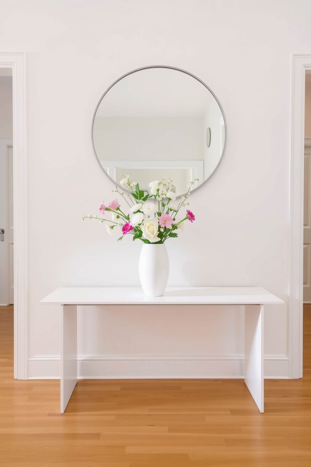 A simple white vase filled with fresh flowers sits elegantly on a sleek console table. The flowers add a touch of color and vibrancy to the otherwise minimalist space. The foyer features a bright and airy design with white walls and a polished wooden floor. A large round mirror hangs above the console, reflecting natural light and enhancing the welcoming atmosphere.